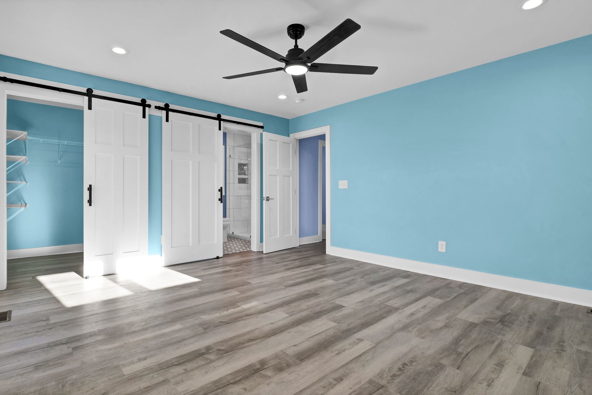 An empty room with blue walls and a ceiling fan.