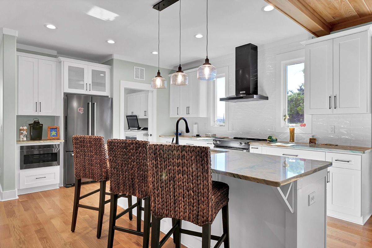 A kitchen with white cabinets, stainless steel appliances, a large island, and wicker chairs