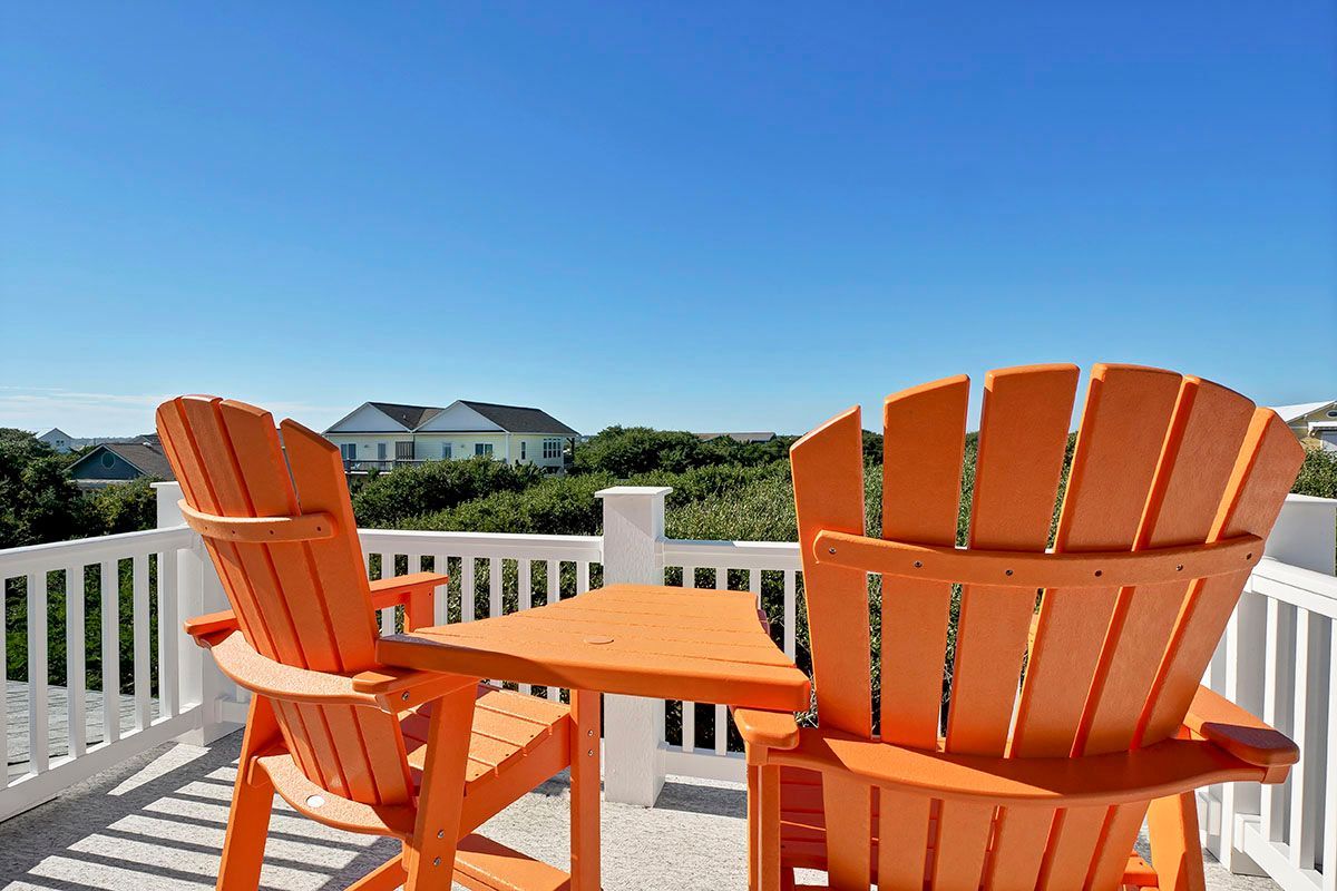 Two orange wooden chairs and a table on a deck overlooking the ocean