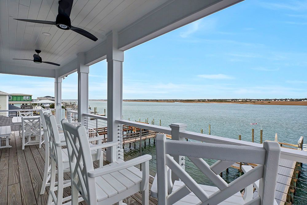 A porch with chairs and a ceiling fan overlooking a body of water