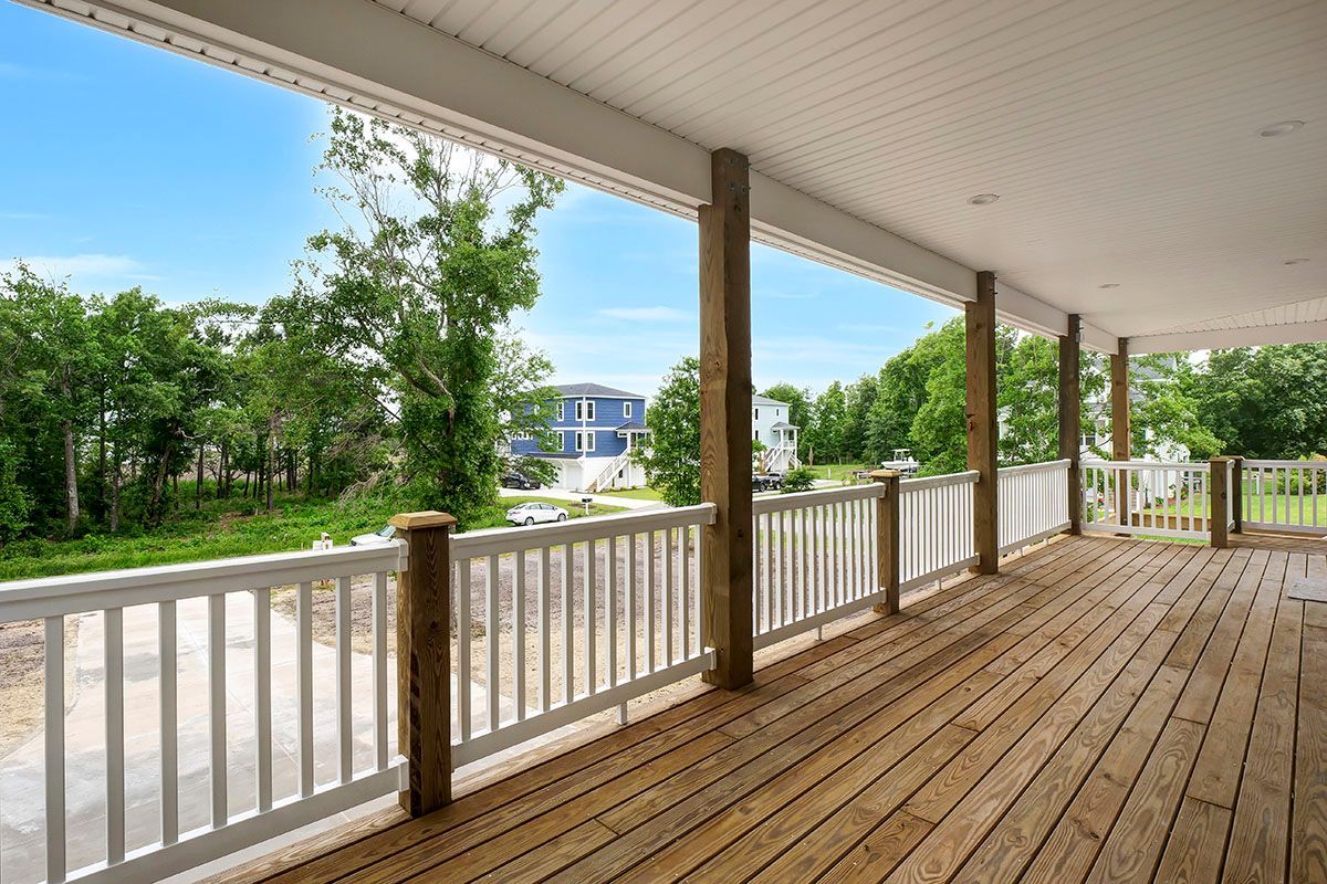 A large wooden deck with a white railing and trees in the background