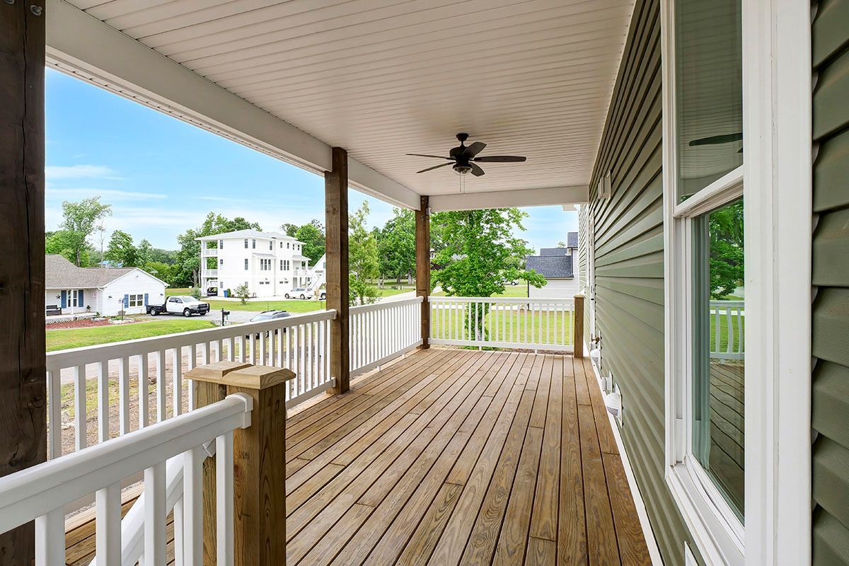 A large wooden porch with a white railing and a ceiling fan