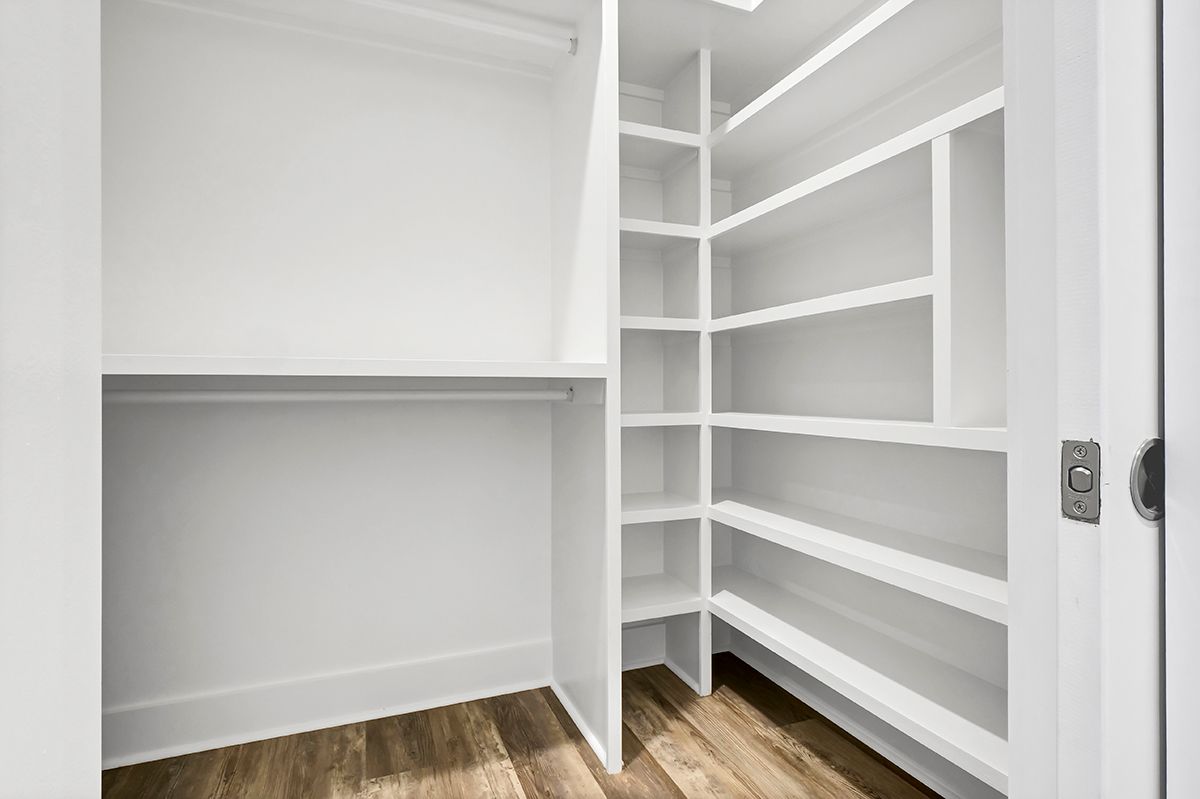 An empty walk-in closet with white shelves and wooden floors