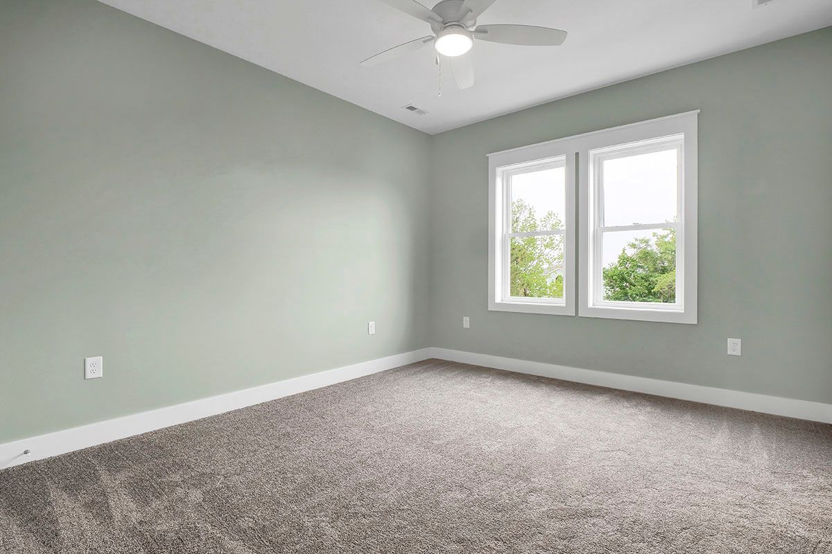 An empty bedroom with a ceiling fan and windows