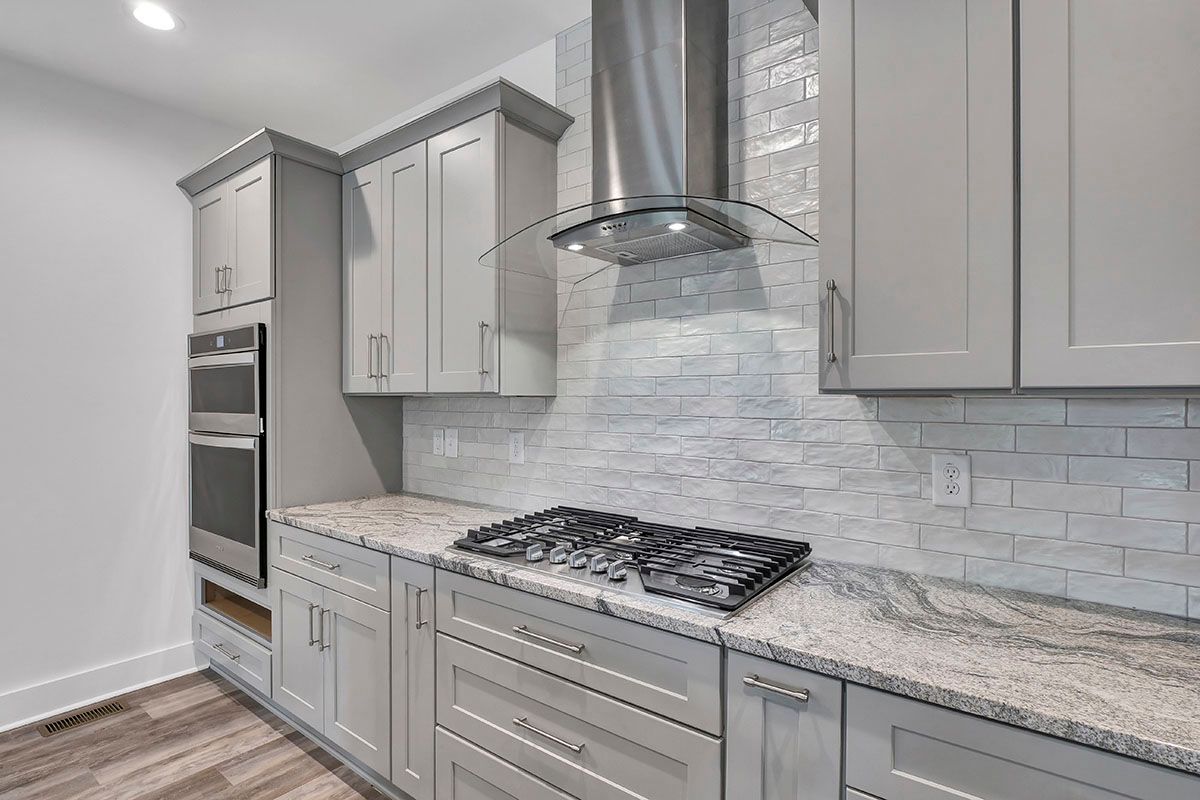 A kitchen with gray cabinets, granite countertops, stainless steel appliances, and a stove-top oven