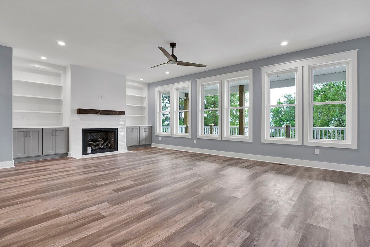 An empty living room with hardwood floors, a fireplace, and a ceiling fan