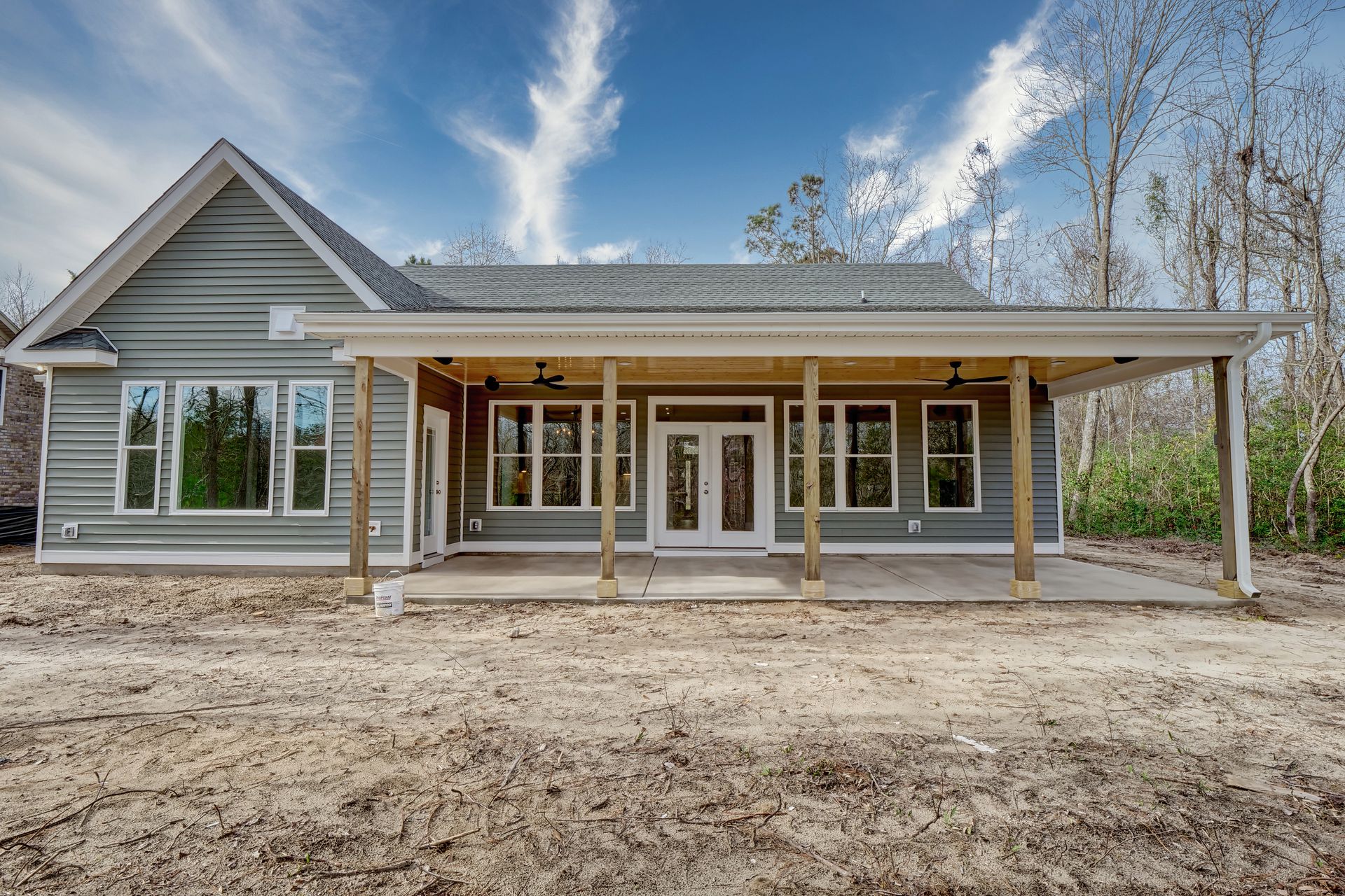 A house with a porch and a lot of windows is sitting on top of a dirt field.