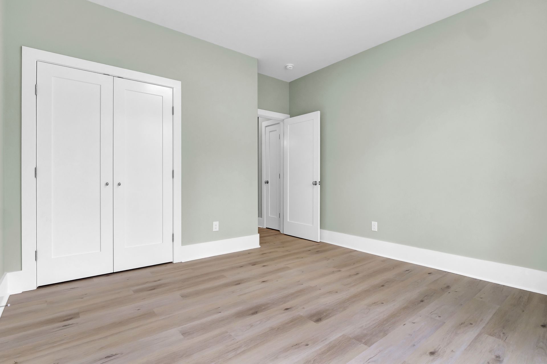 An empty bedroom with hardwood floors and white walls.