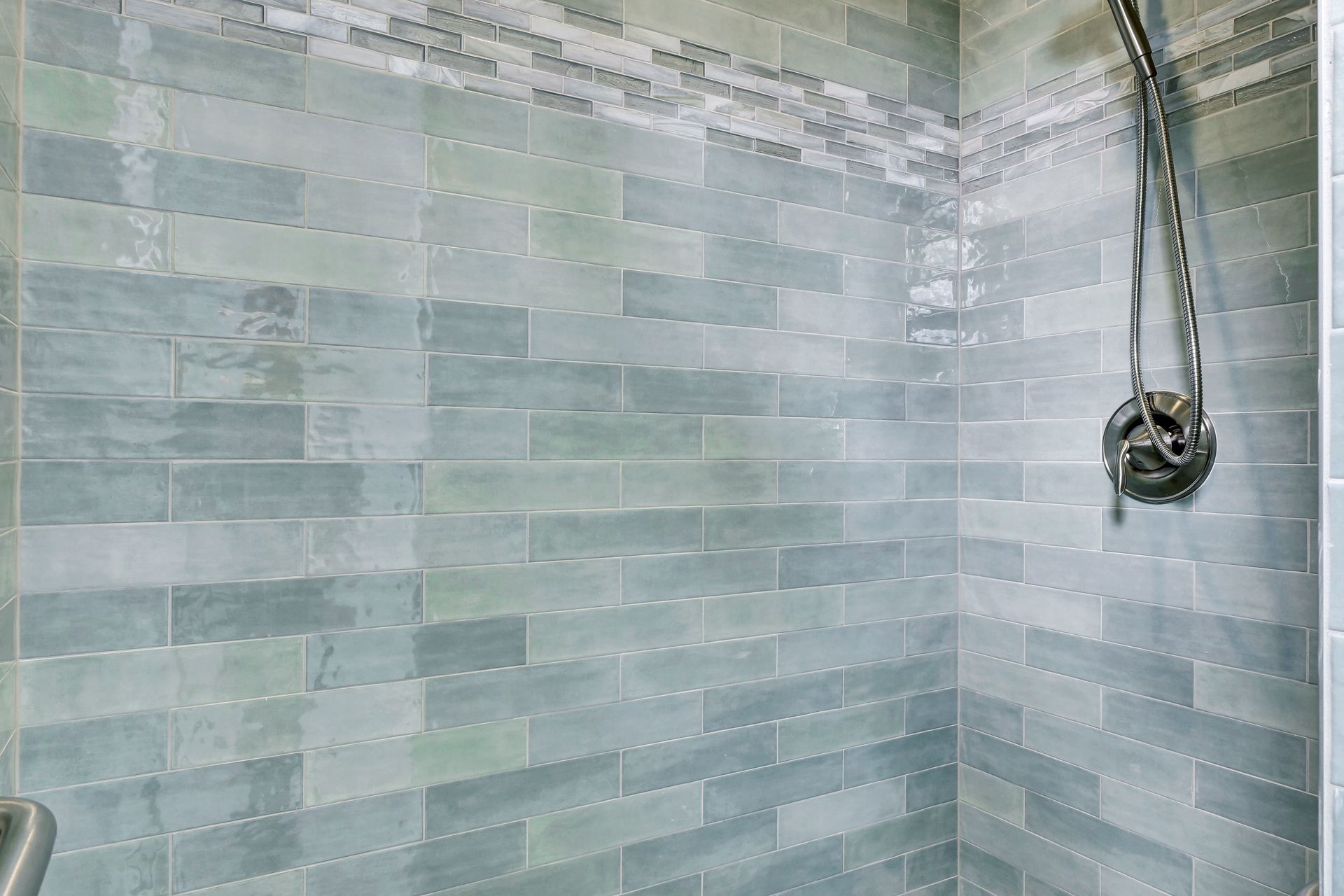 A shower with blue tiles and a shower head hanging from the wall.