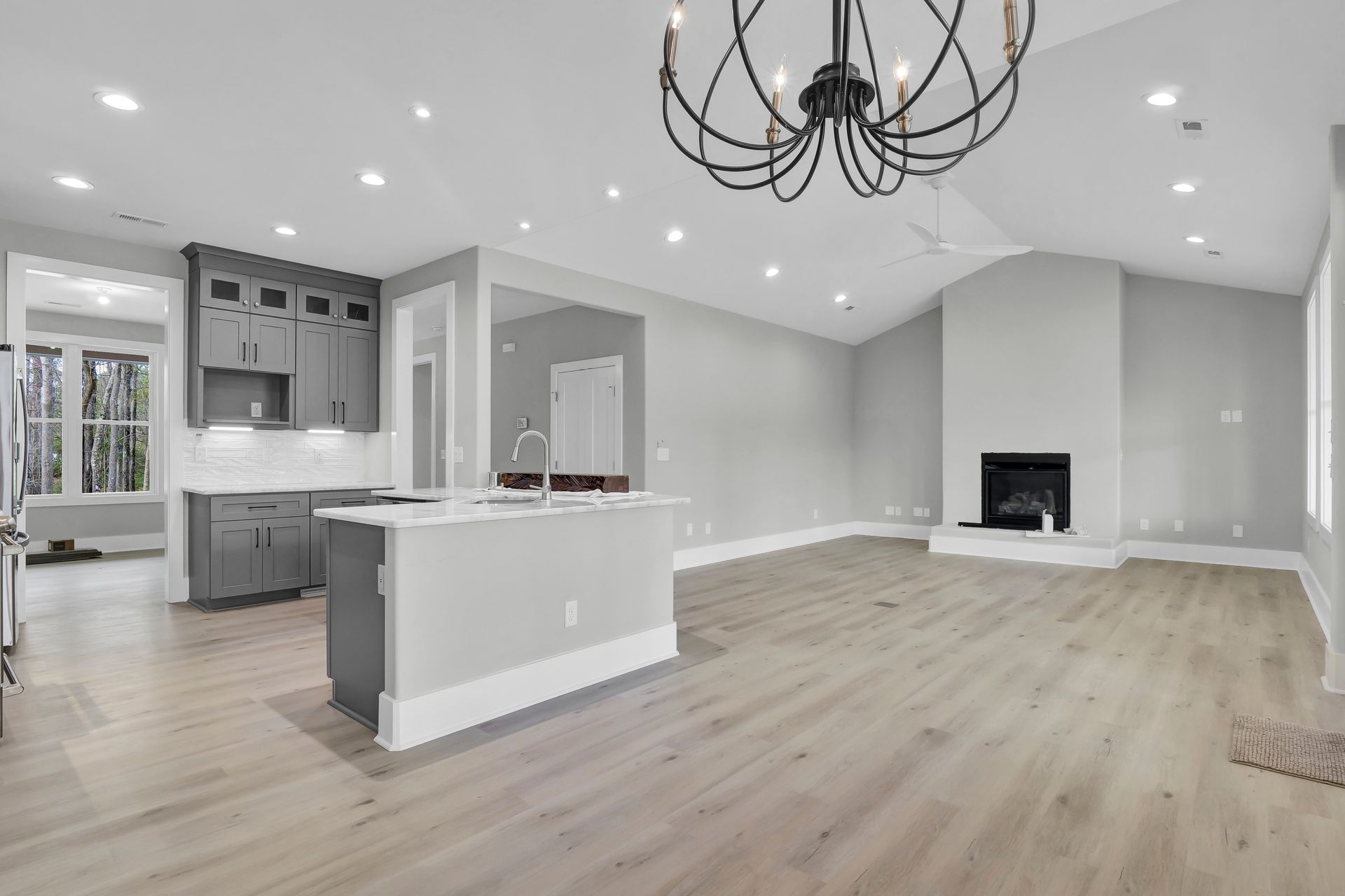 An empty living room with hardwood floors and a chandelier hanging from the ceiling.