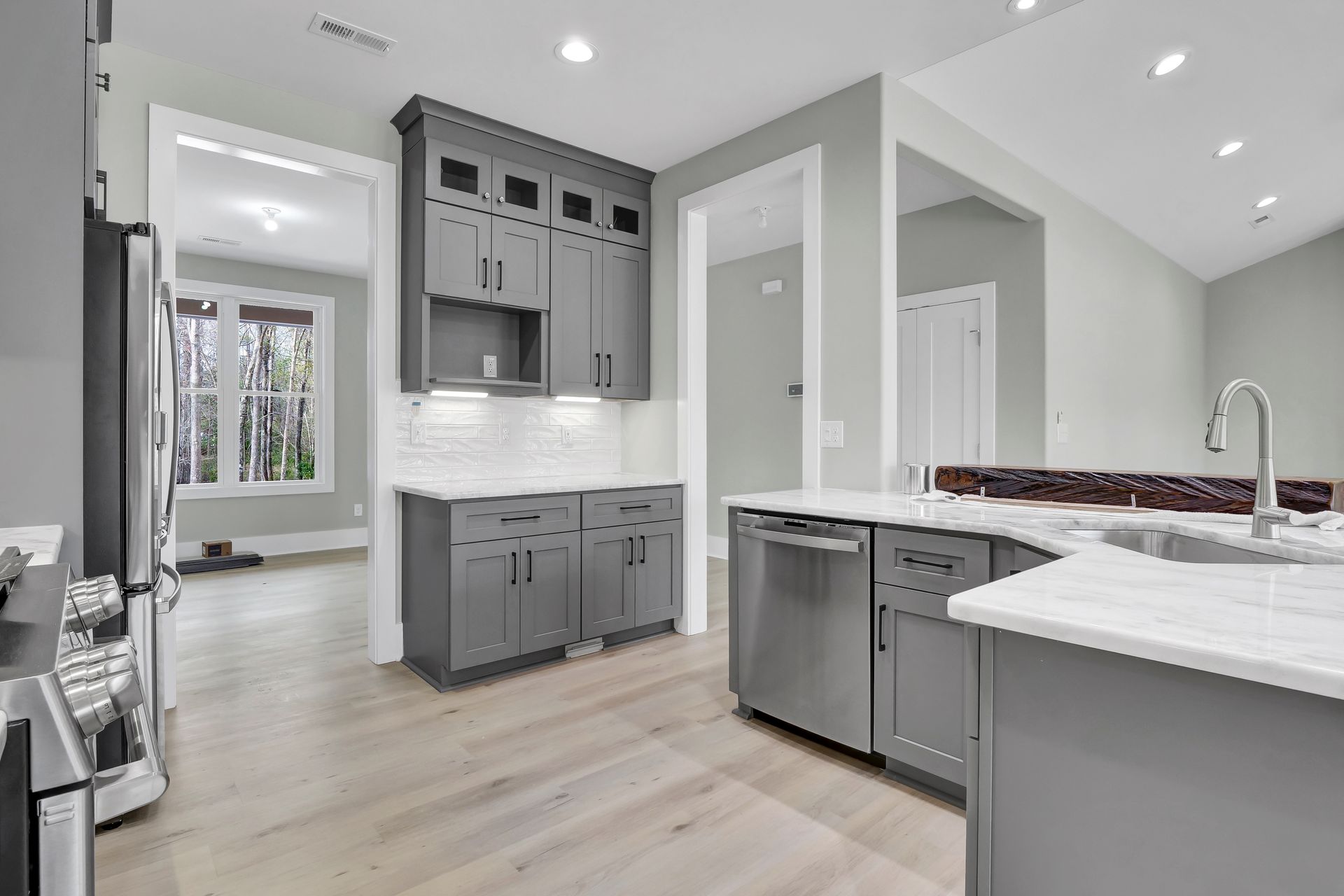 A kitchen with gray cabinets , stainless steel appliances , a sink , and a refrigerator.