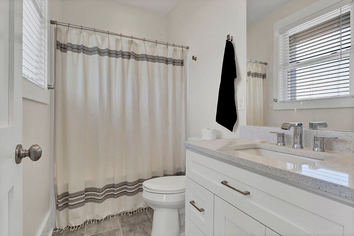 A bathroom with a toilet, sink, shower curtain, and window