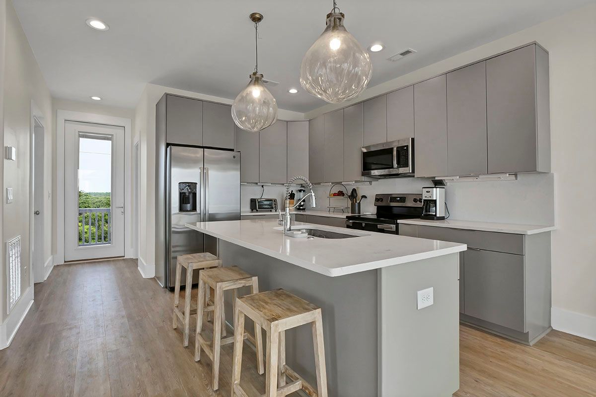 A kitchen with gray cabinets, stainless steel appliances, a large island, and stools