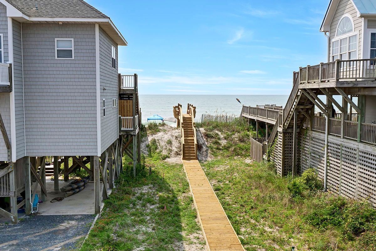 A wooden walkway that leads to the beach between houses