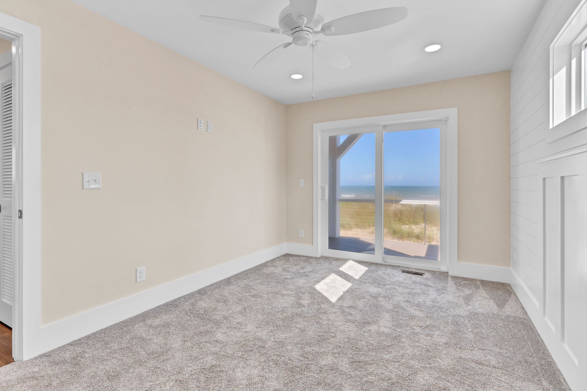 An empty room with a ceiling fan , sliding glass doors , and a view of the ocean.