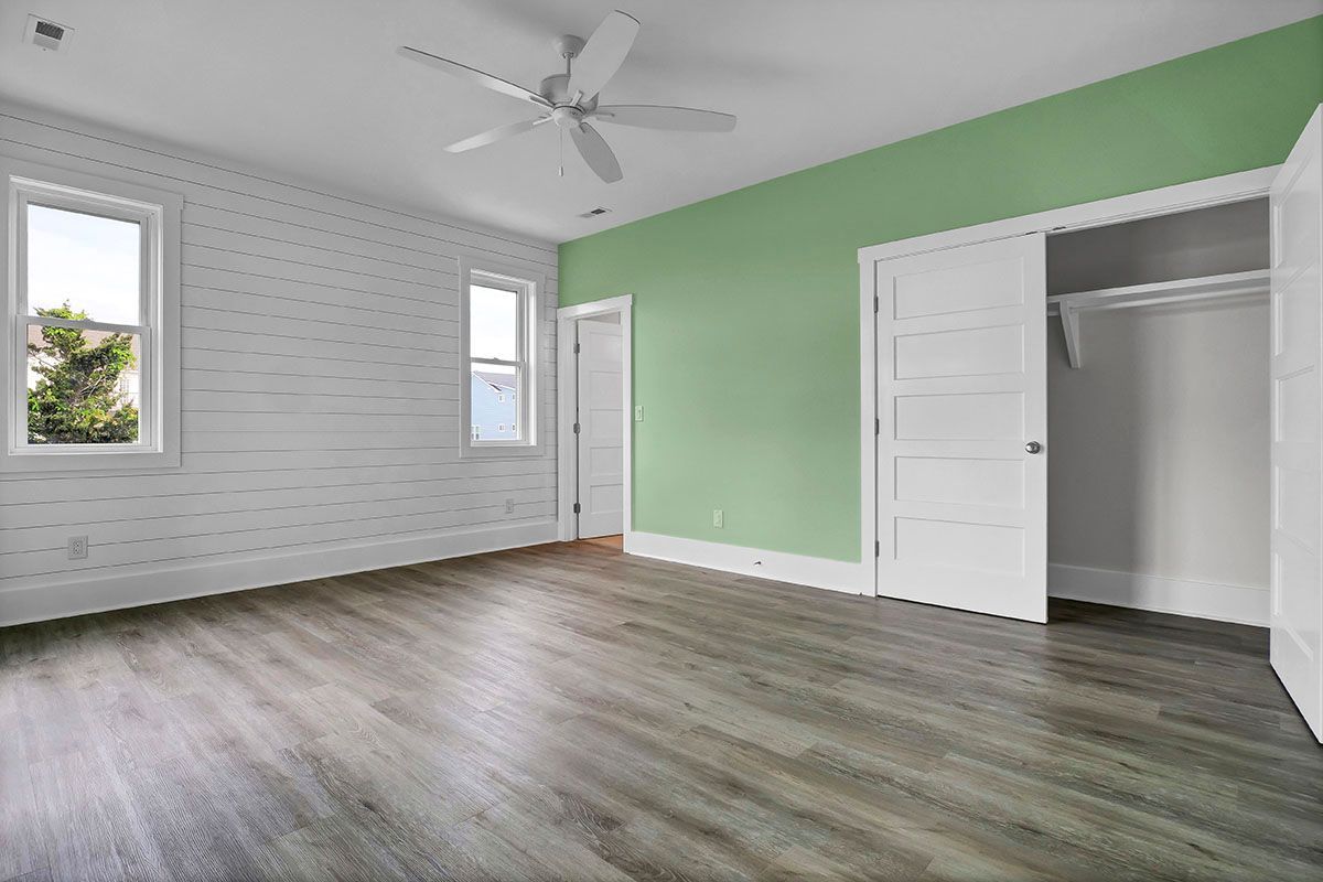 An empty bedroom with green walls and a ceiling fan