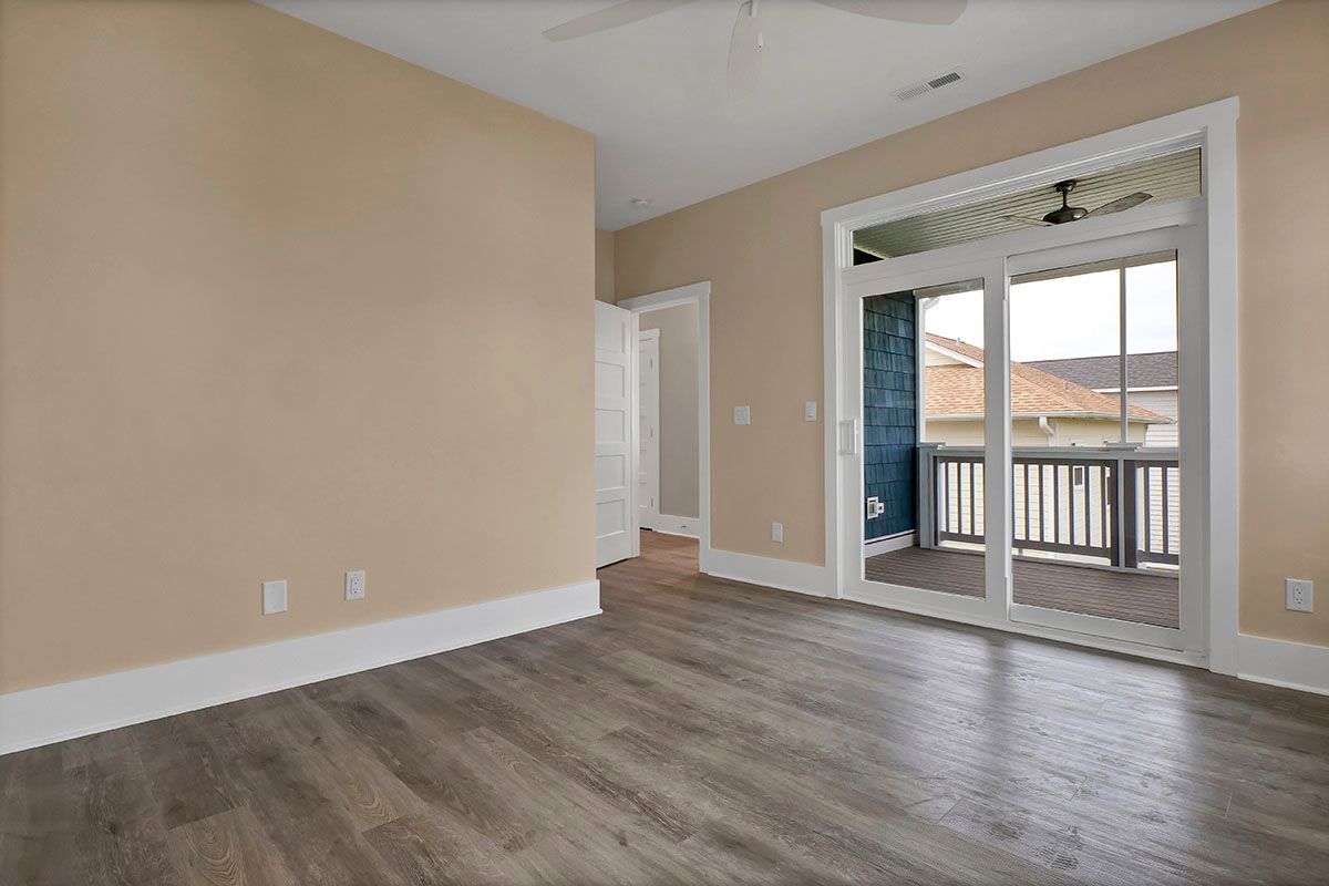 An empty room with hardwood floors and sliding glass doors leading to a balcony