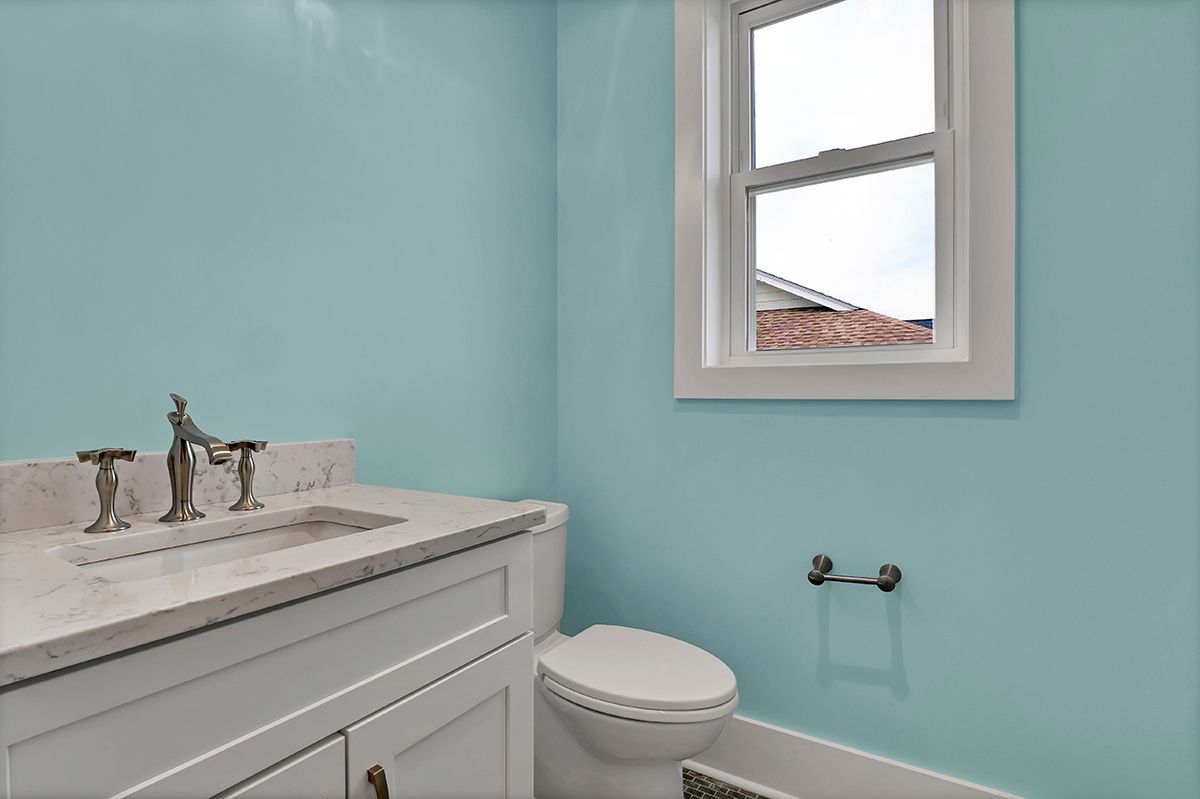 A bathroom with blue walls, a toilet, a sink, and a window