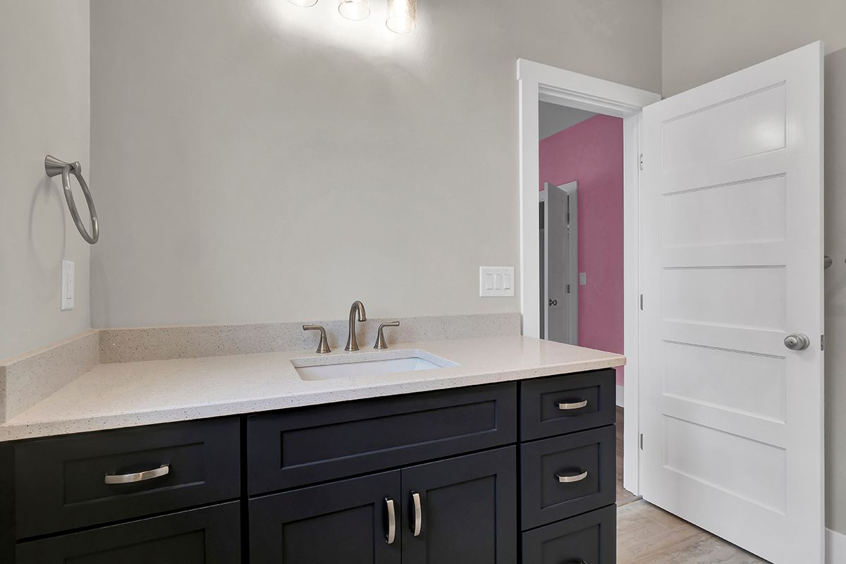 A bathroom with a sink, cabinets, drawers, and a door