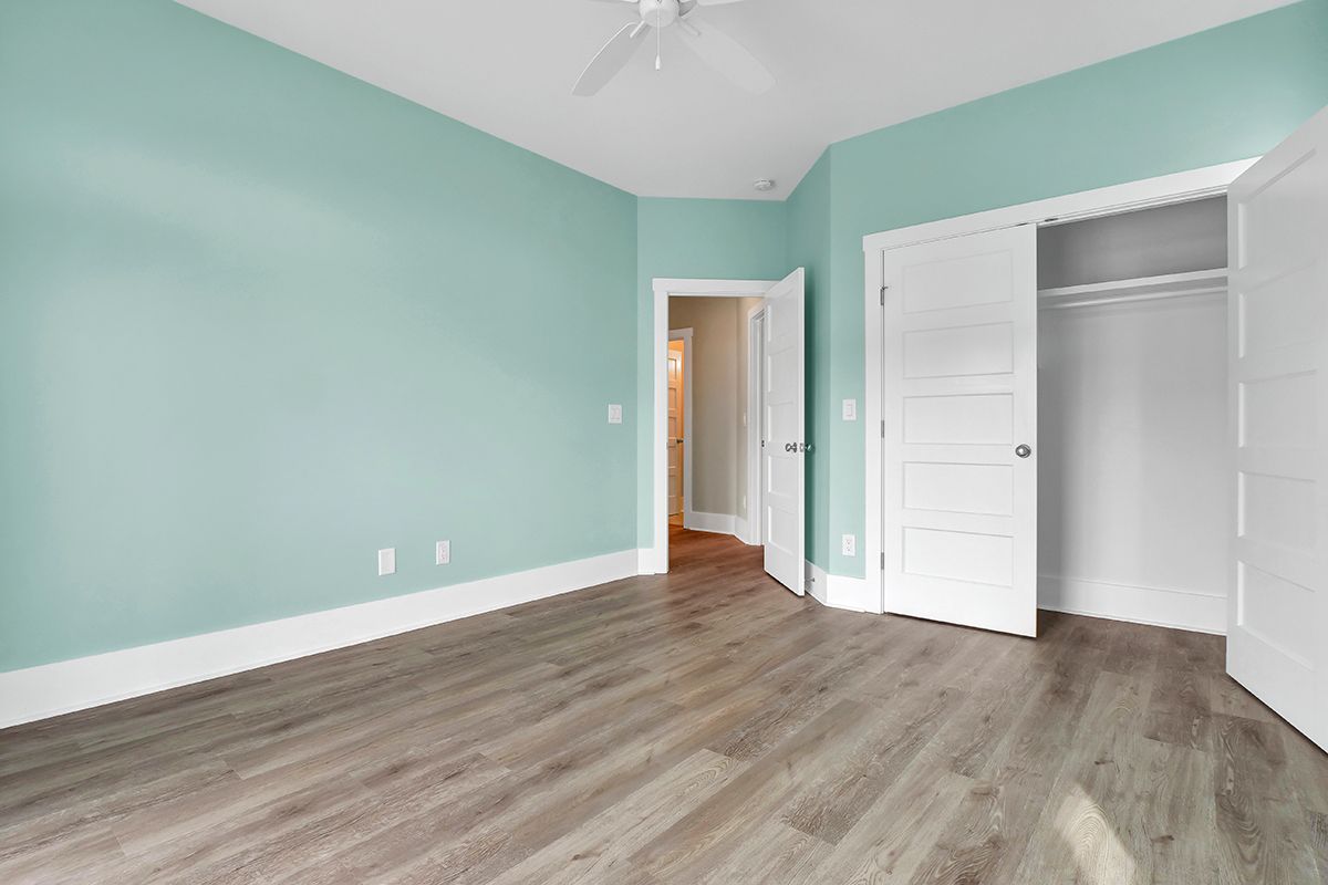 An empty bedroom with green walls, wooden floors, and a ceiling fan
