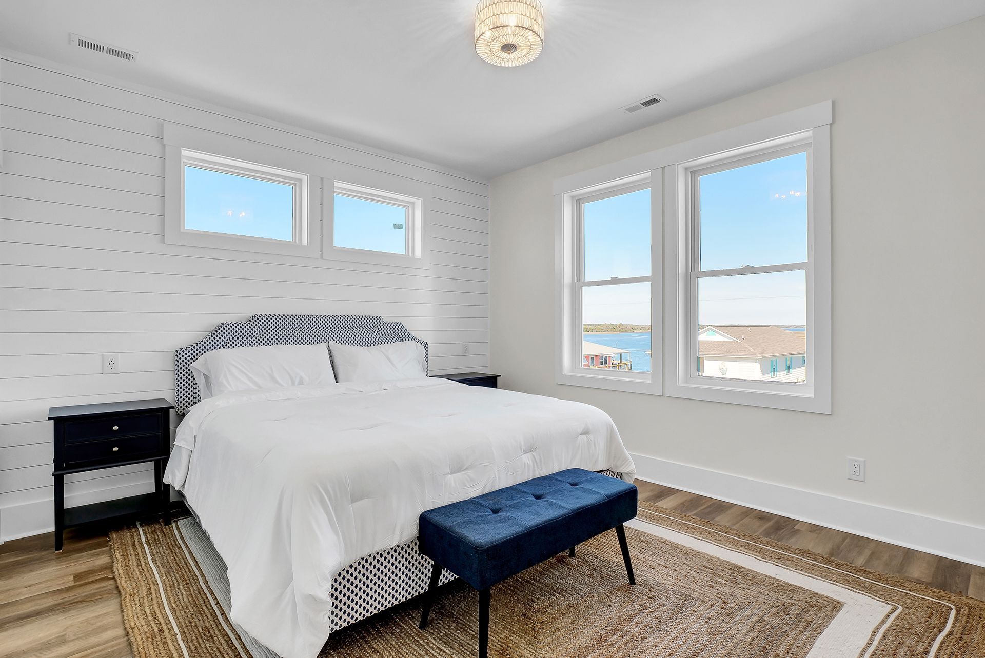 A bedroom with a bed, two nightstands, a bench, and windows