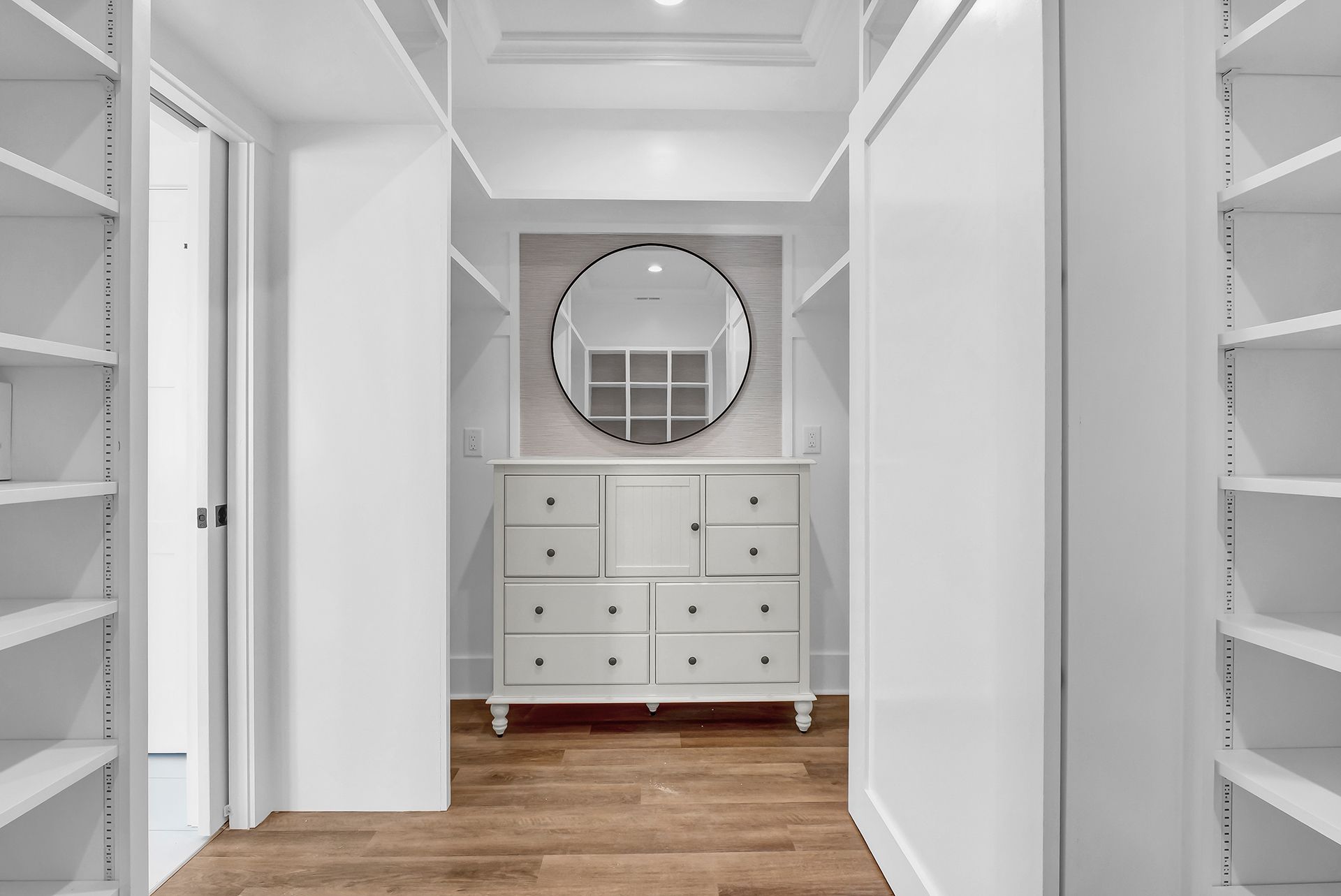 A walk-in closet with a round mirror and a lot of shelves and drawers