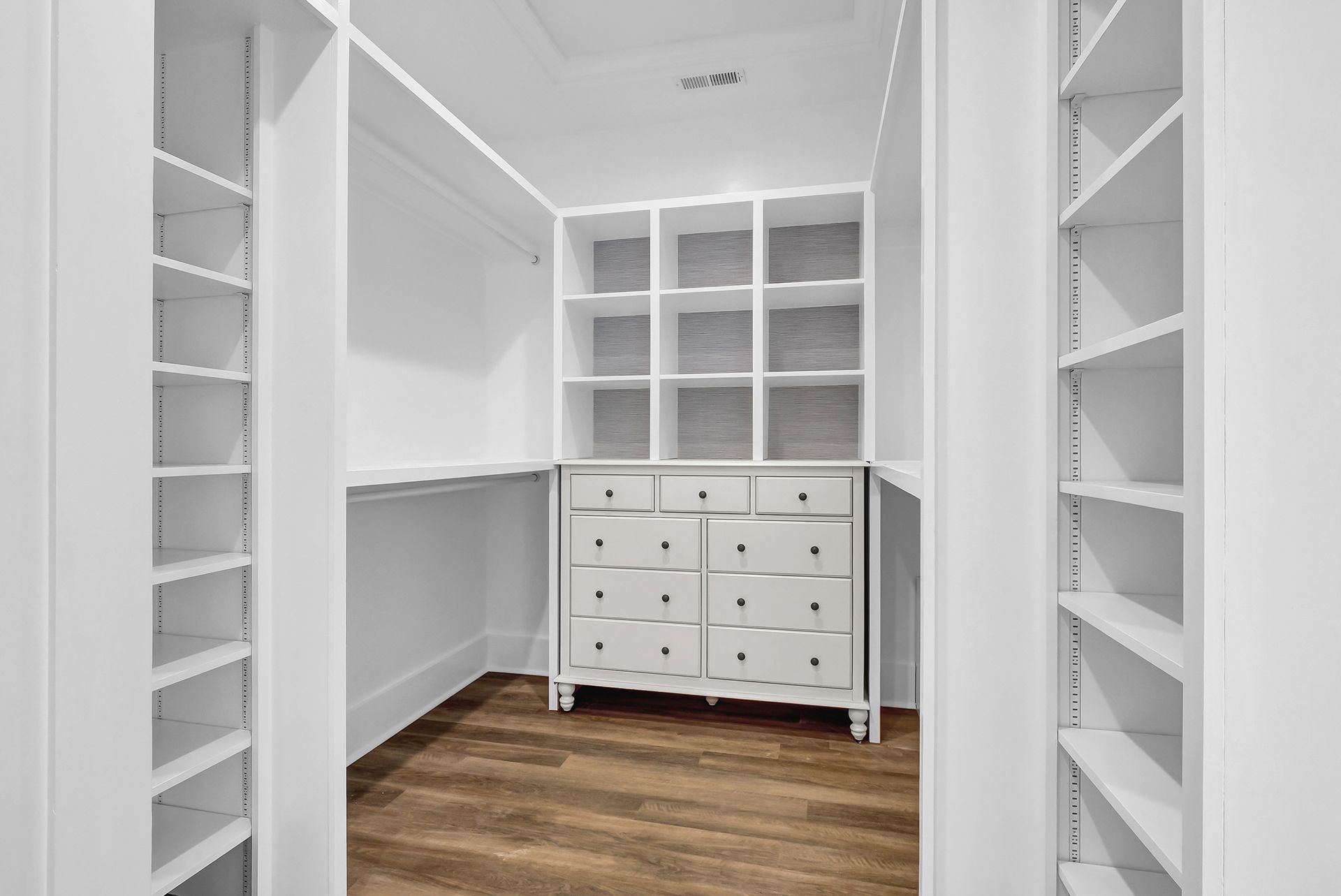 A walk-in closet with white shelves and a dresser