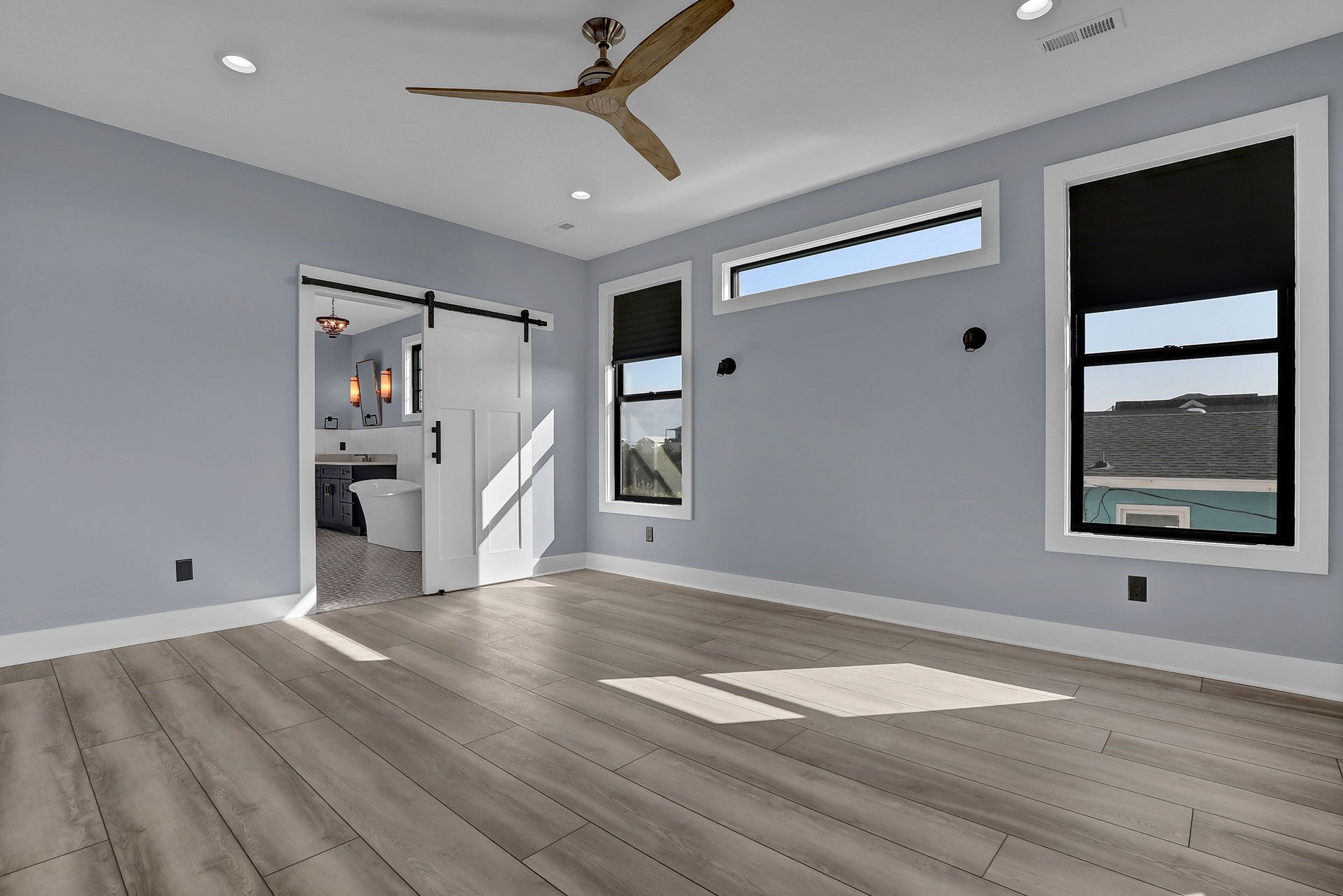 Bedroom with grey walls, wood-look floor, white trim, and sliding barn door to bathroom.
