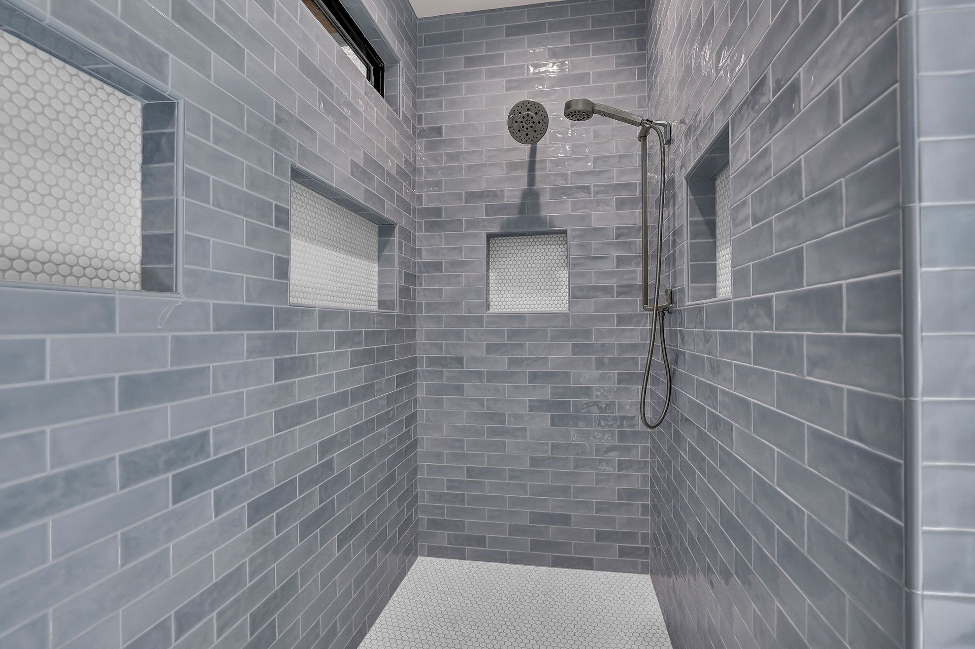Blue tiled shower with a shower head and recessed niches.