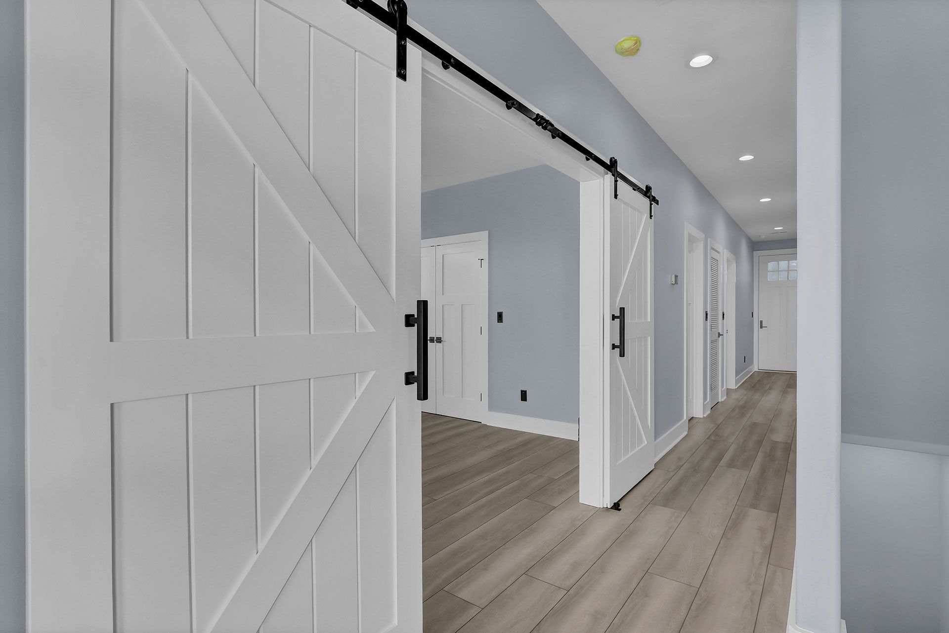 White barn doors open to a hallway with light wood flooring and blue walls.