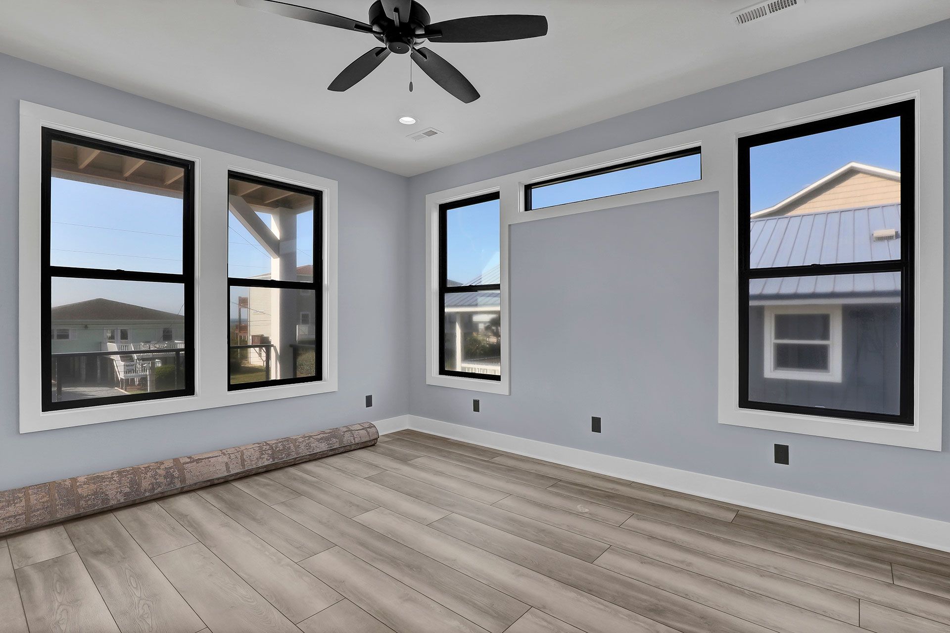 Empty bedroom with hardwood floors, several windows, light blue walls, and a ceiling fan.