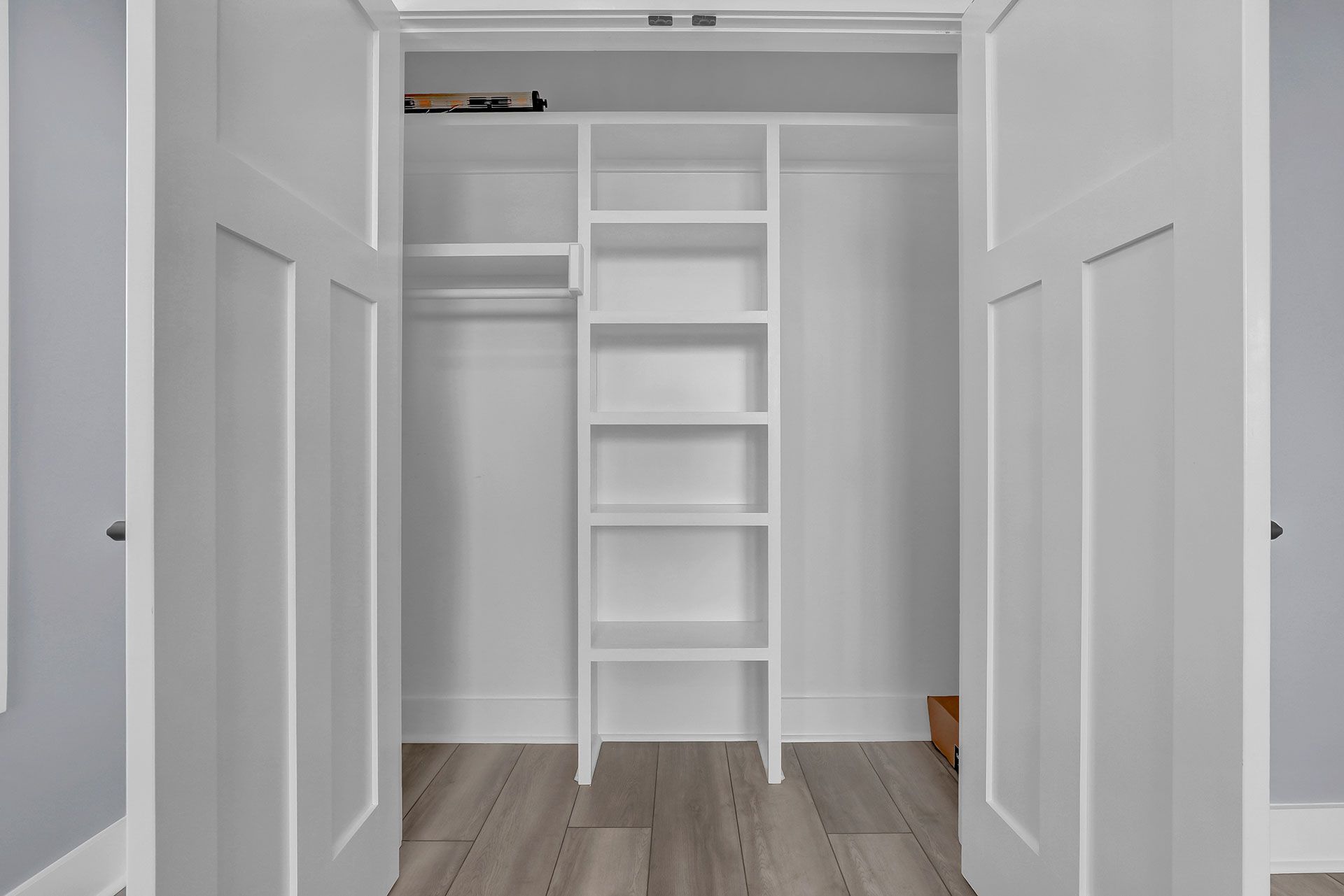 White closet with open doors, shelves, and a clothes rod, on a wood-look floor.