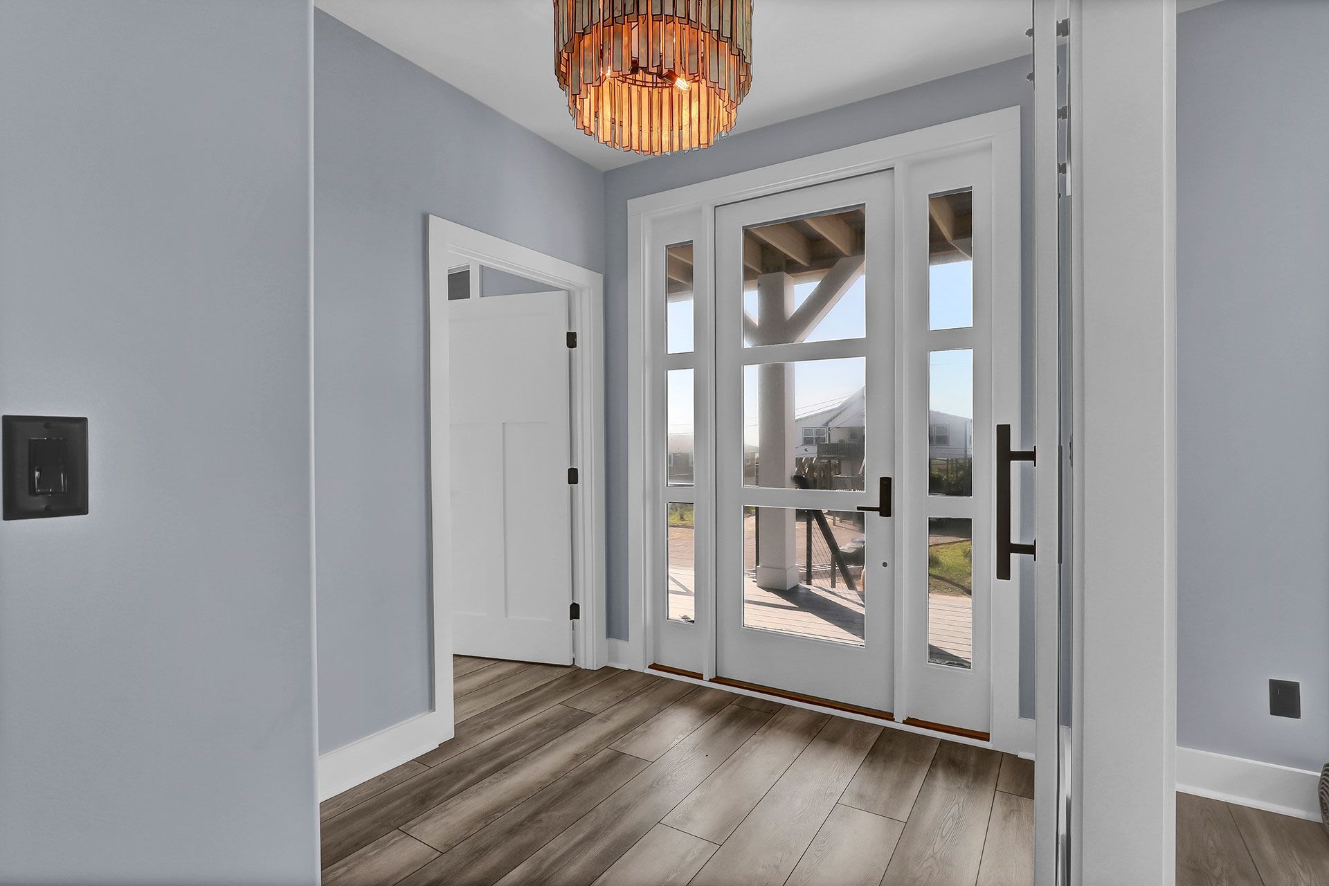 Entryway with light blue walls, wooden floor, and glass doors leading to an outdoor view.