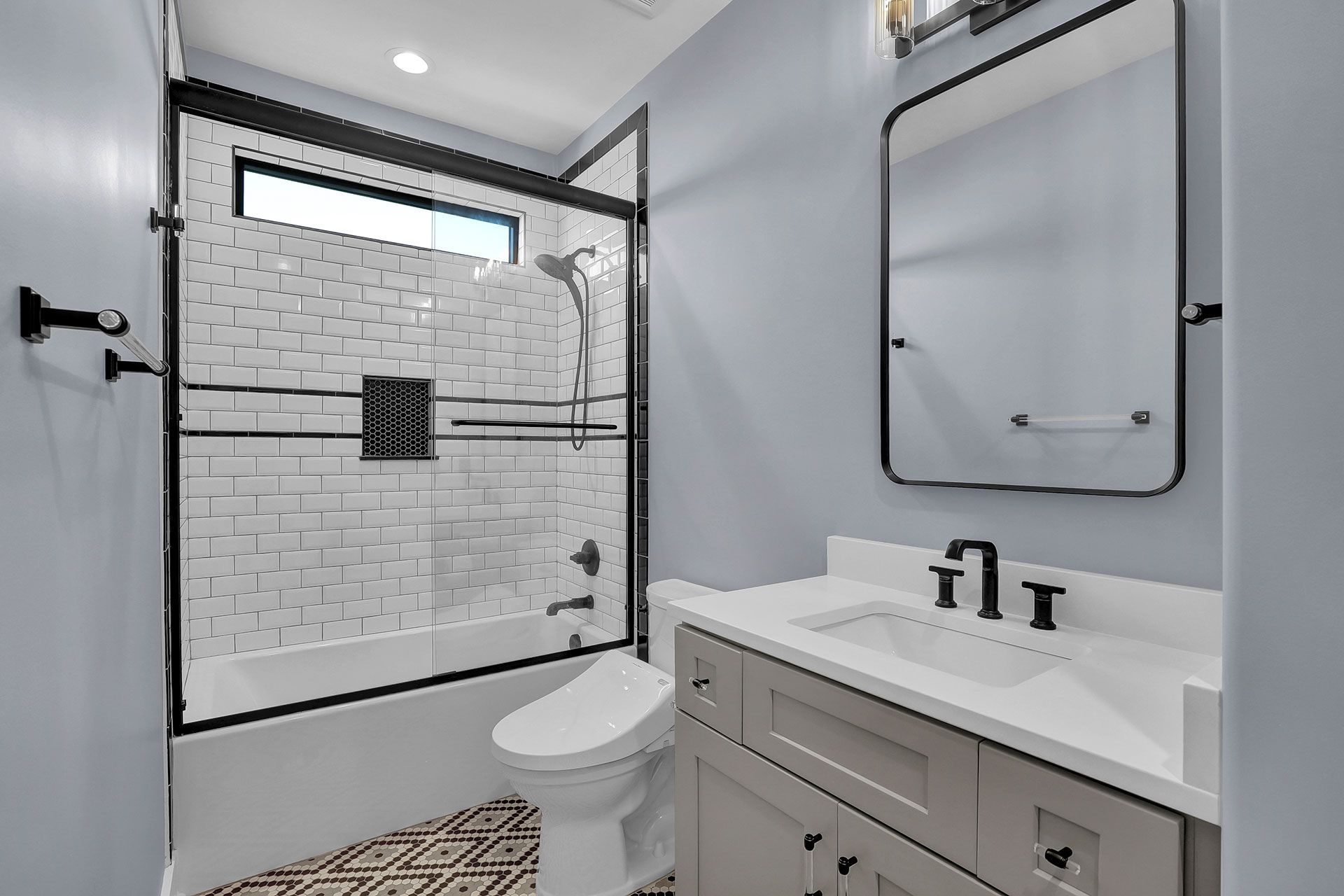 A modern bathroom with a gray vanity, white sink, and black framed shower.