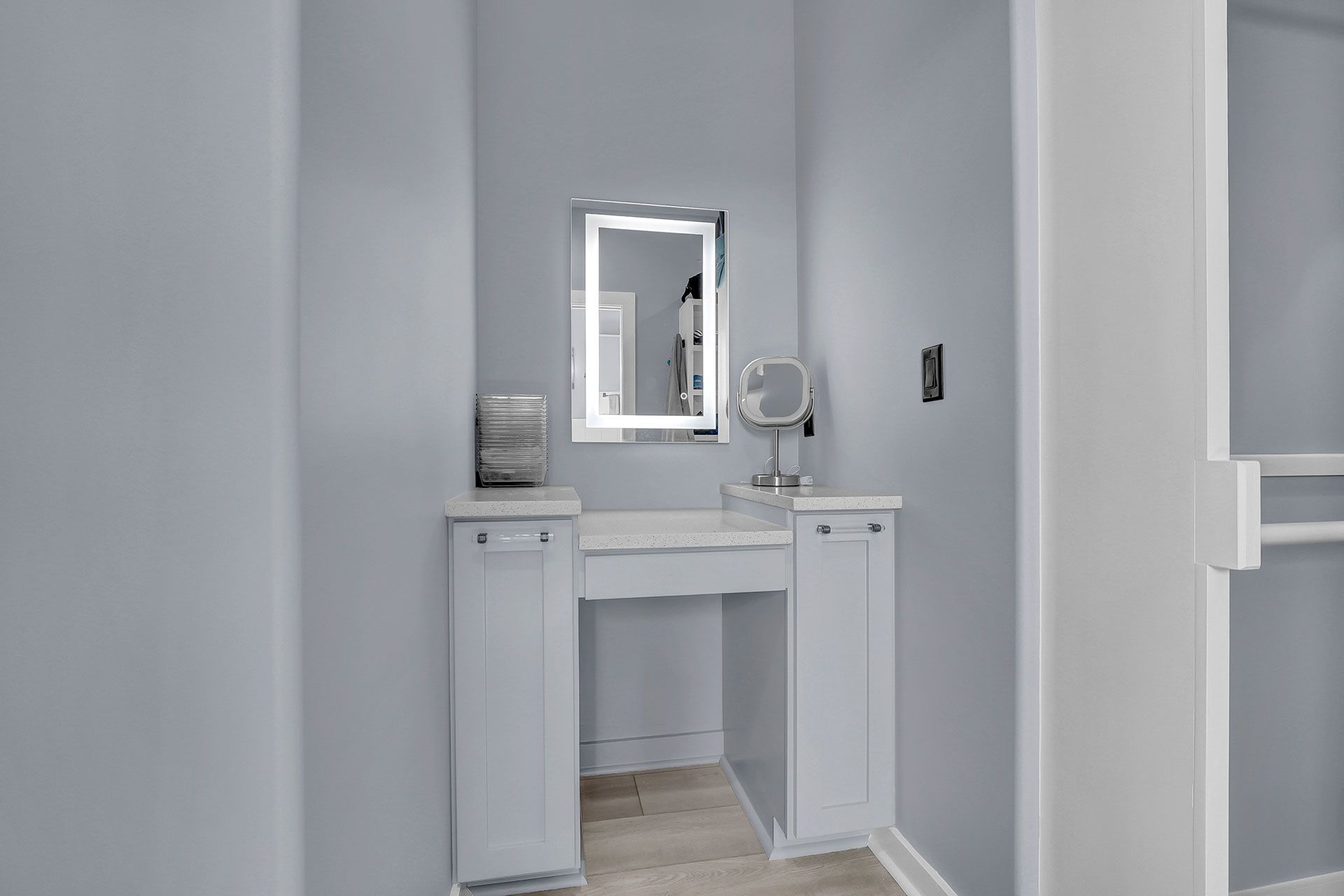 A built-in white vanity with a lit mirror in a light blue alcove.
