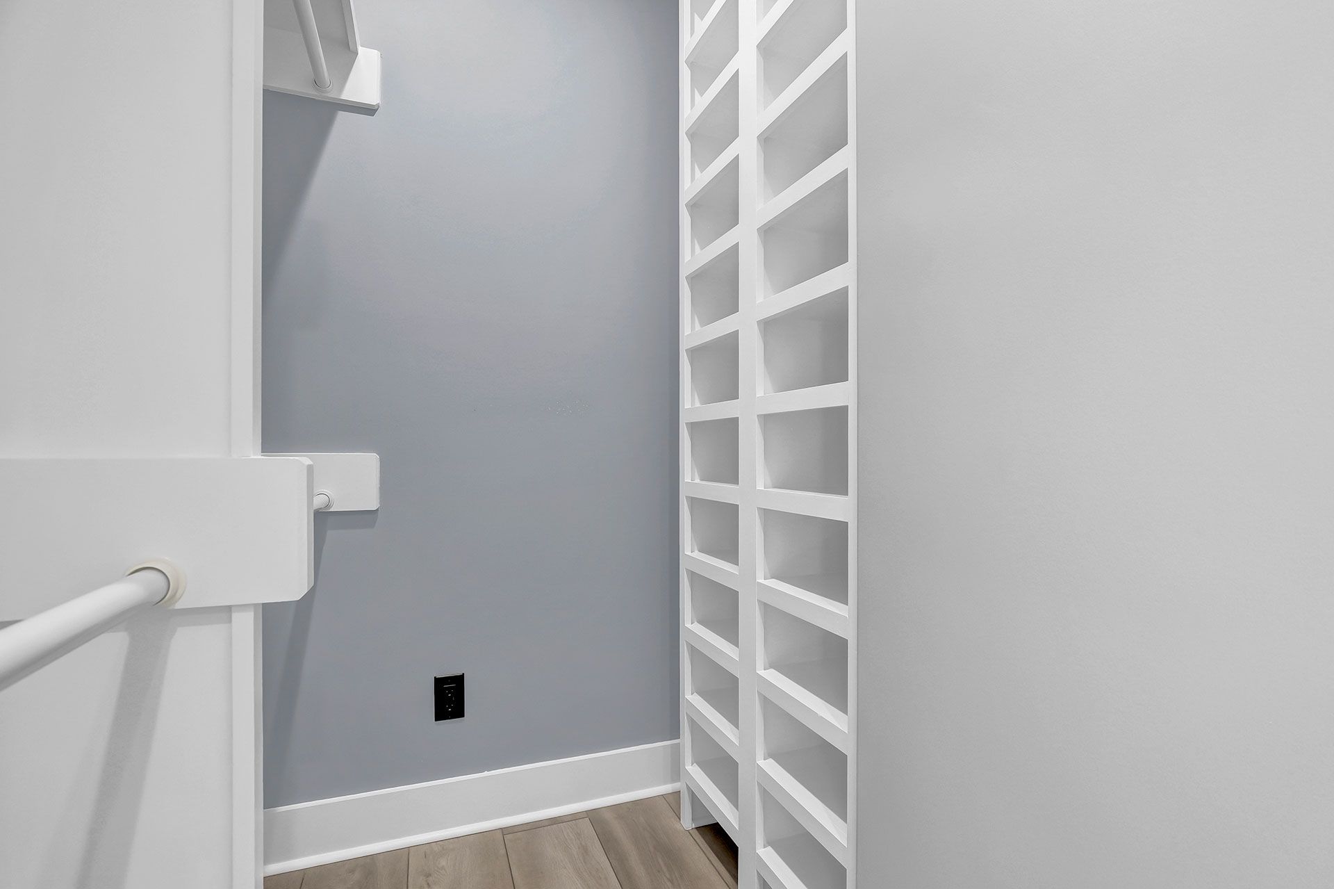 Small, white closet with built-in shelves on the right, gray wall, and wooden floor.