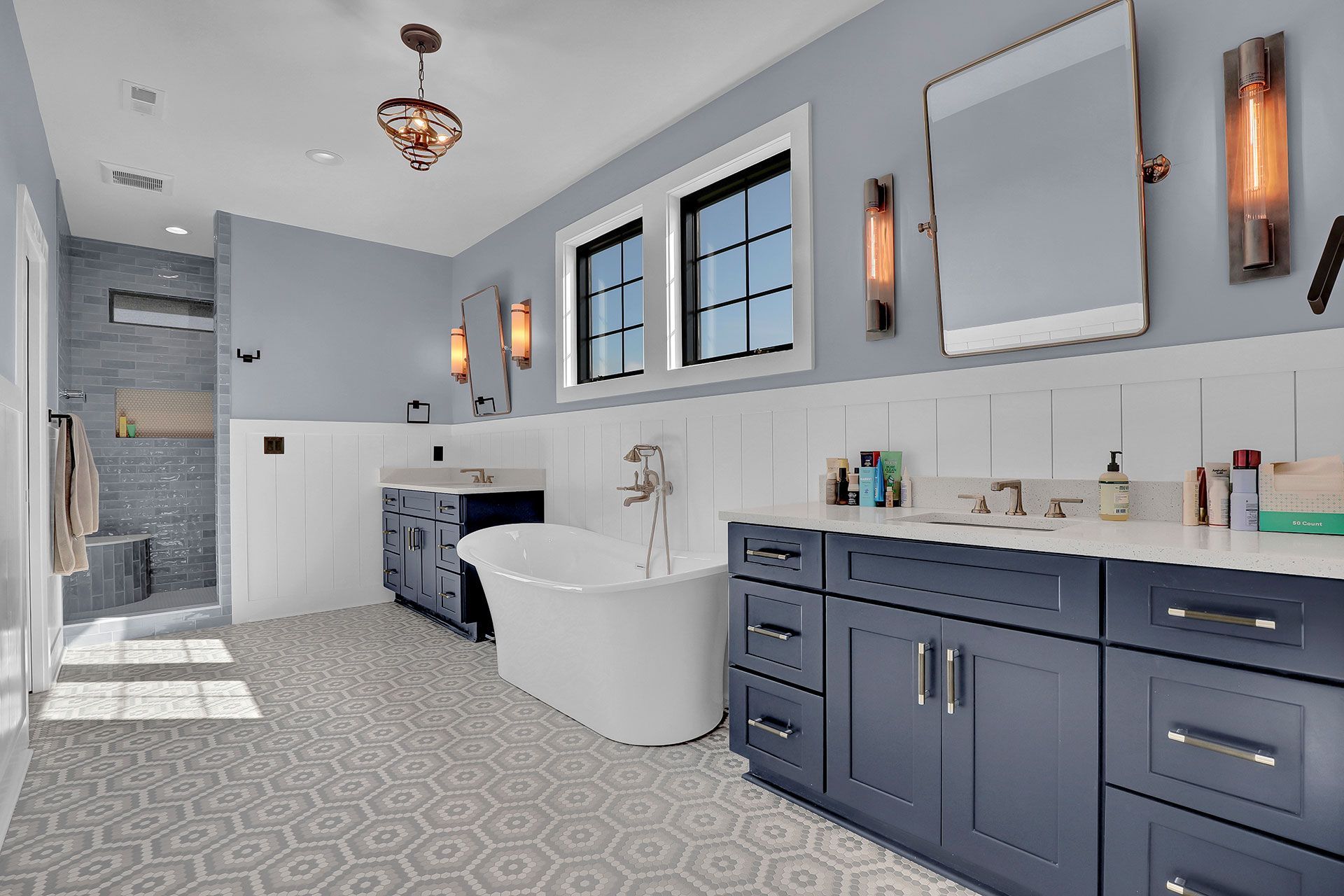 Blue and white bathroom with bathtub, dual sinks, and gray hexagon tiled floor.
