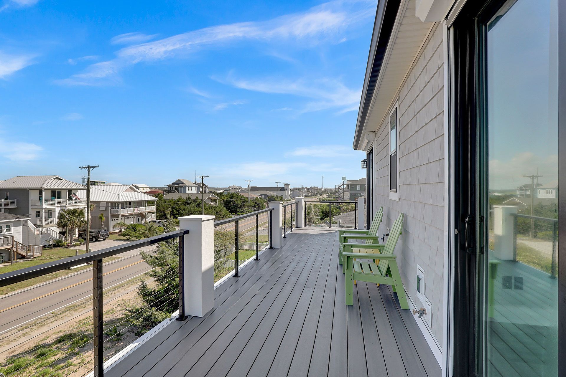 Rooftop deck with gray floor, black railing, green bench, beach houses, and blue sky.
