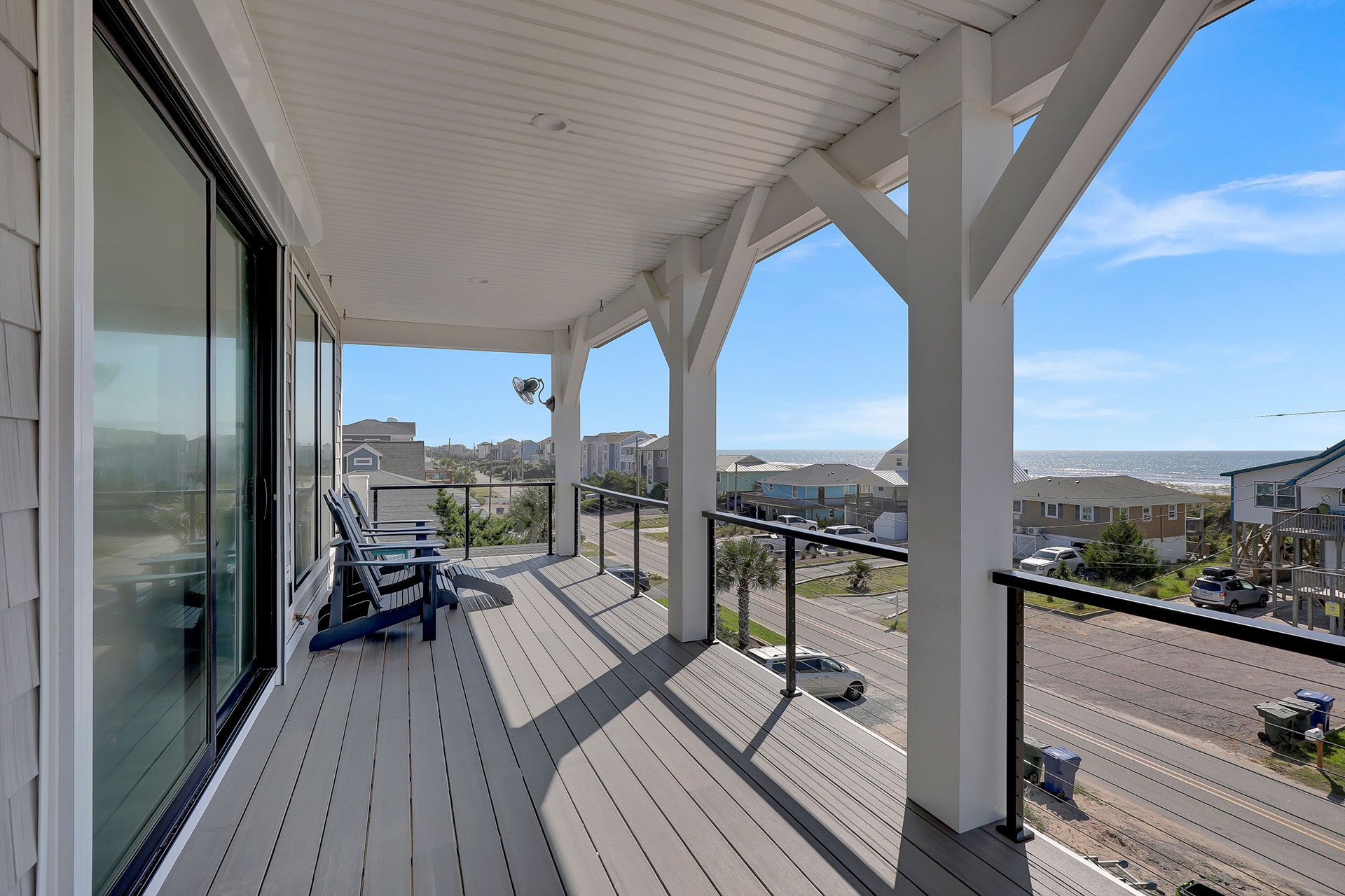 Balcony with ocean view, gray deck, white columns, two blue chairs.