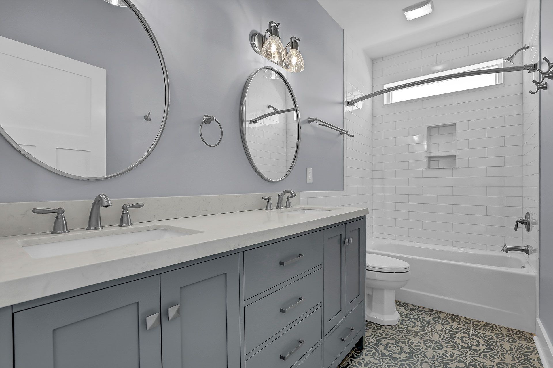 Bathroom with blue vanity, gray walls, two mirrors, and a white tiled shower.