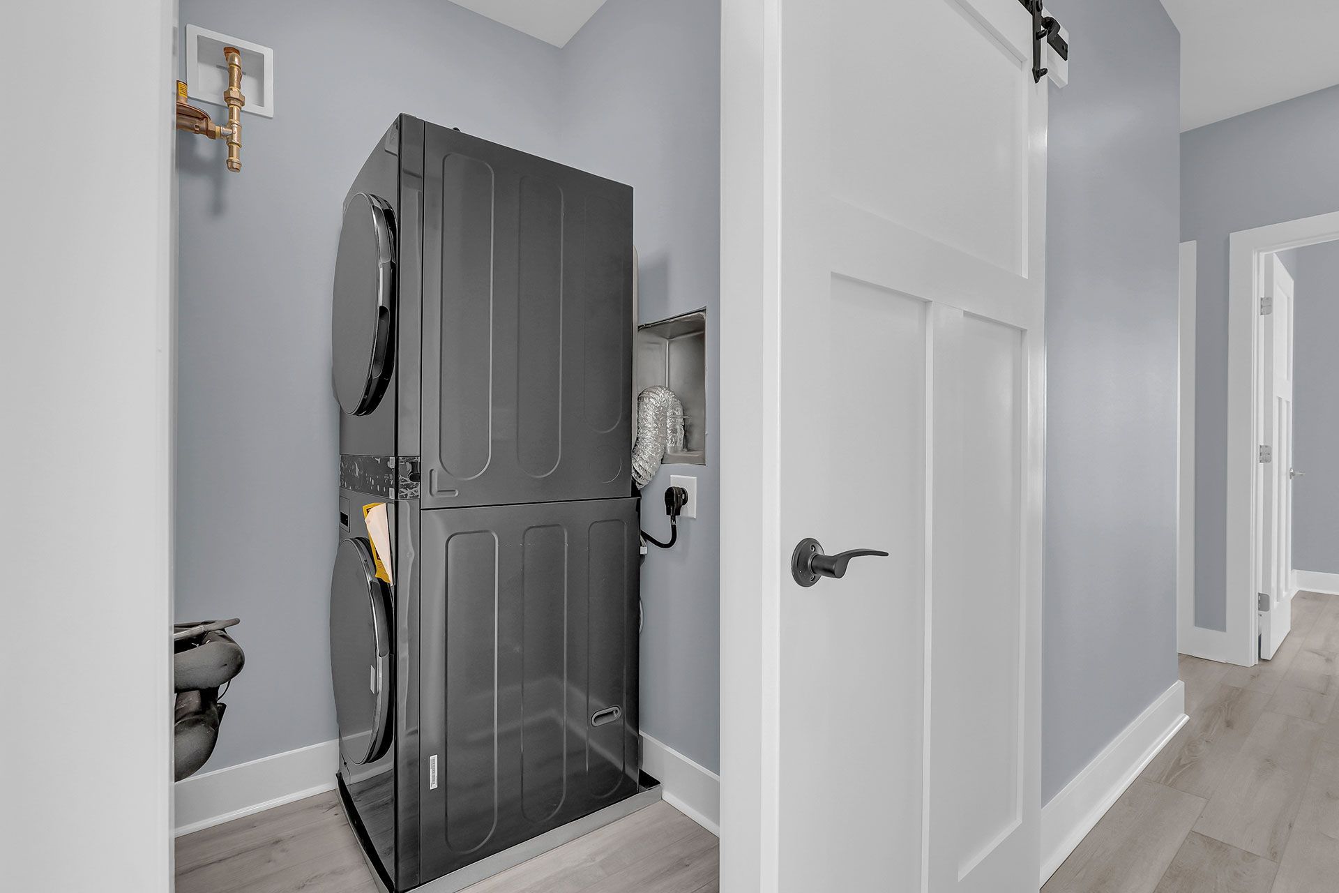 Stacked black washer and dryer in a laundry room with light blue walls and a white door.
