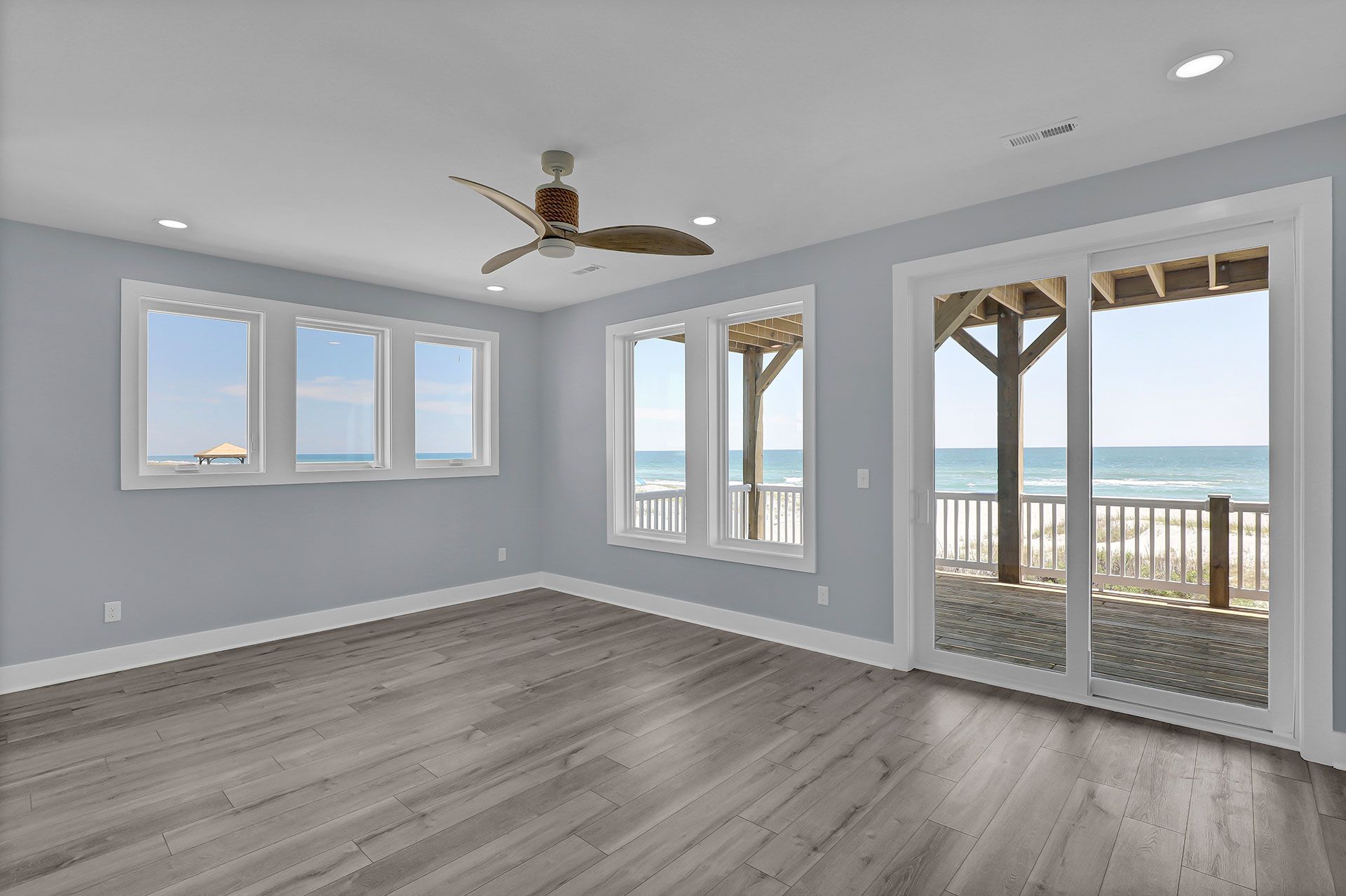 Empty room with ocean view, gray walls, wood floors, and sliding glass doors.