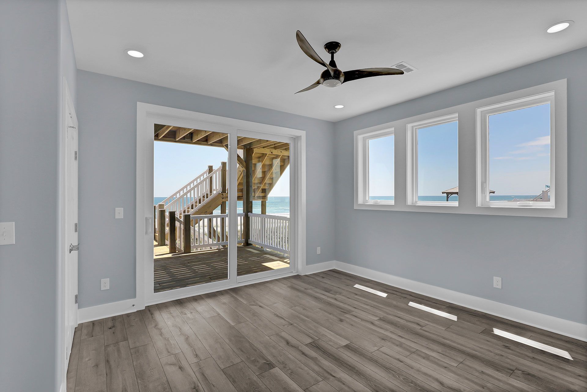 A light-blue room with ocean view; windows, deck, wood floor, ceiling fan.