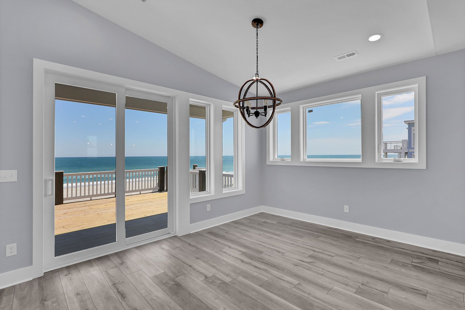 Light blue room with ocean view from windows and sliding glass door. Gray wood floor, decorative light fixture.