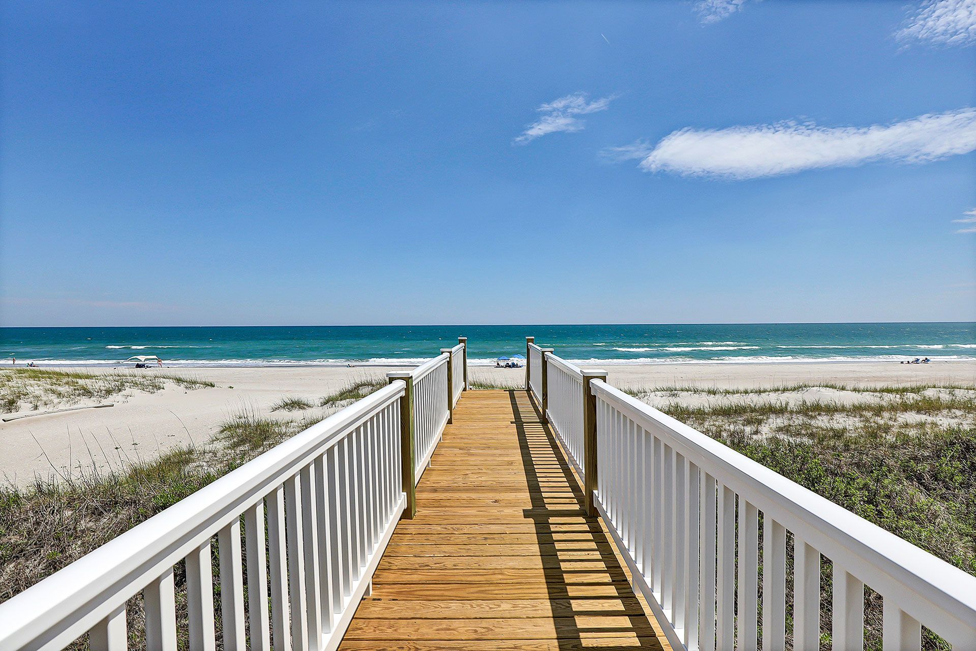 Wooden walkway to a sandy beach with blue ocean under a clear sky.