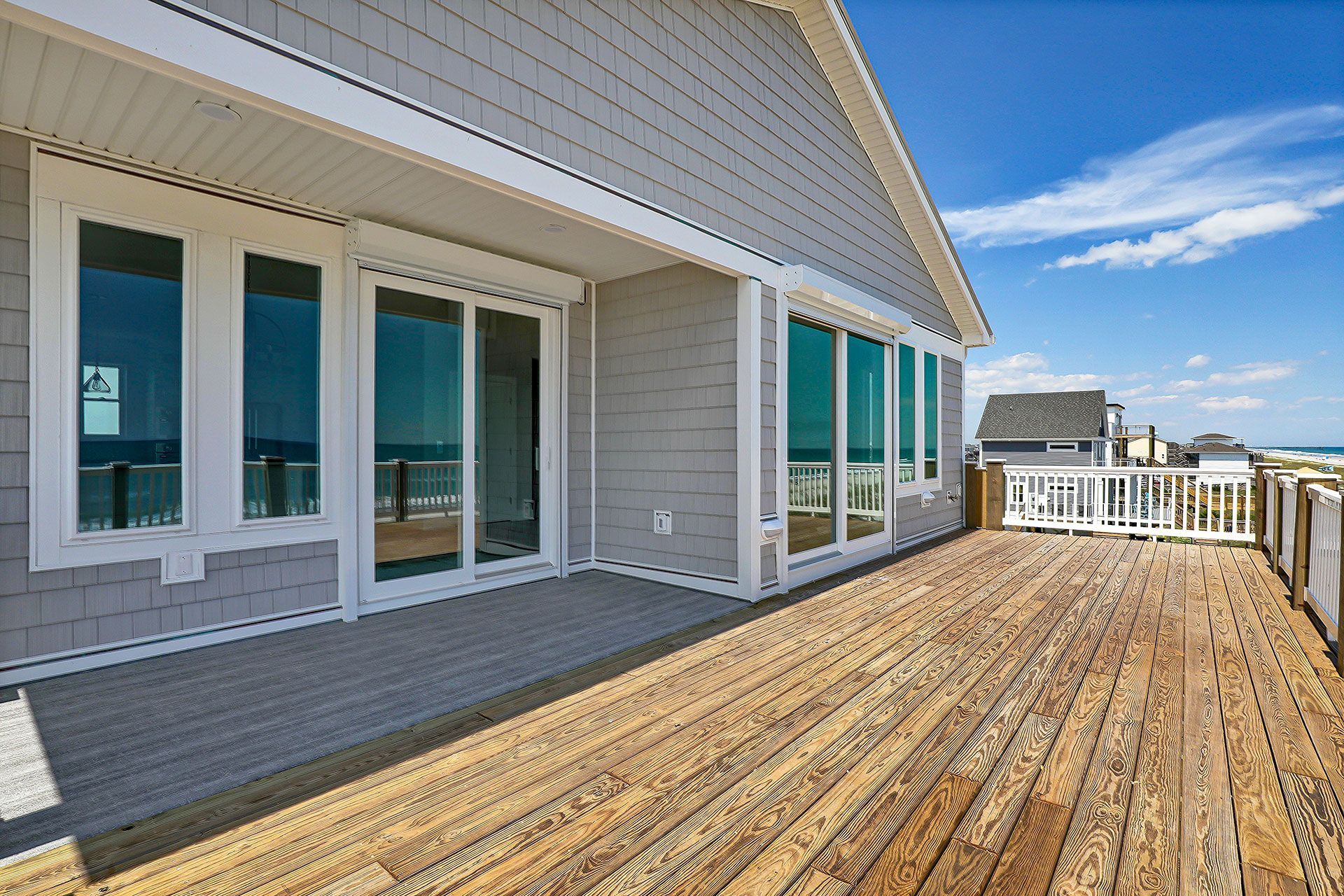 Wooden deck of a light gray house overlooking the ocean, with a blue sky.