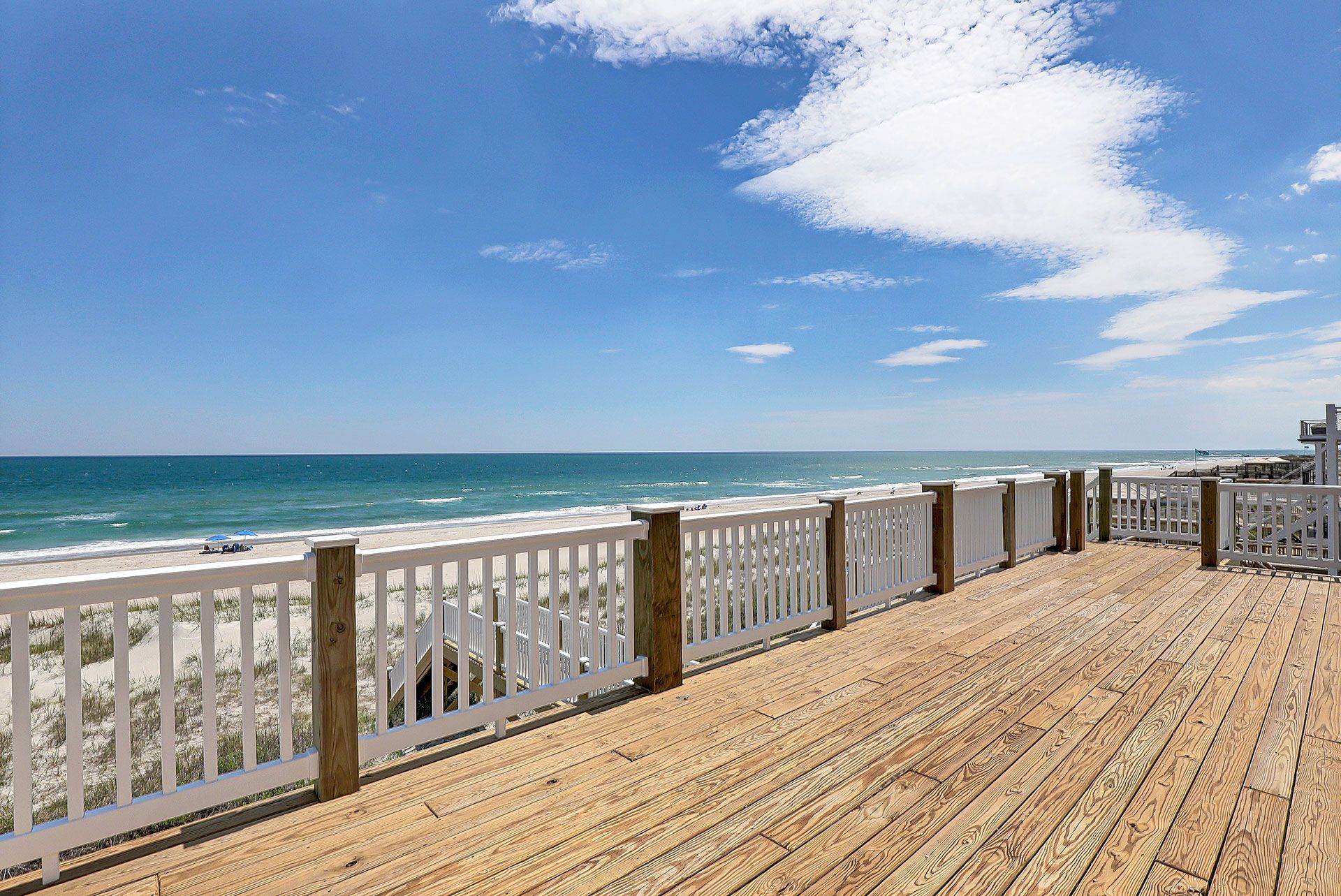 Wooden deck overlooking the beach and ocean on a sunny day with white railings.