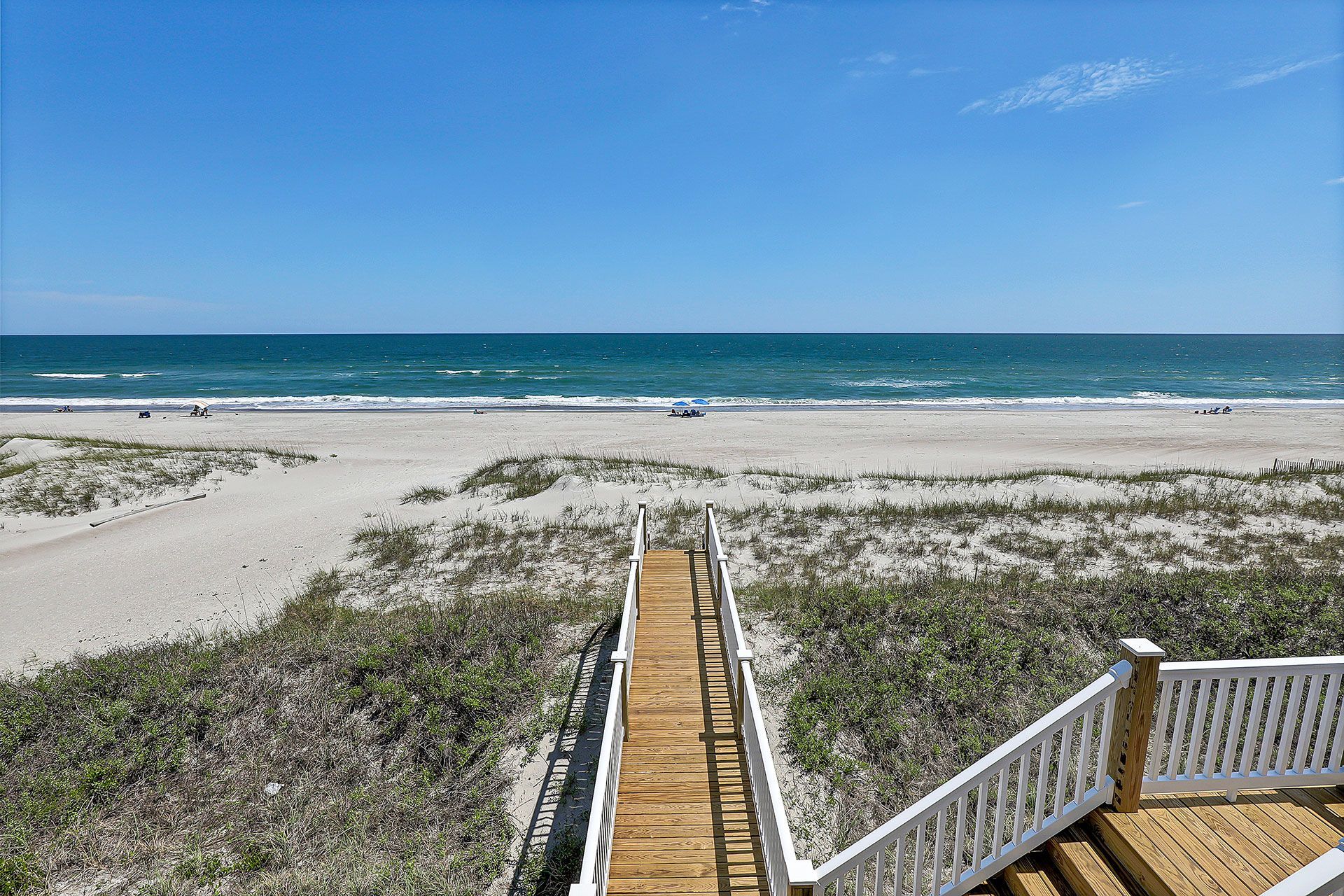 Wooden walkway leading to a sandy beach with ocean view under a blue sky.