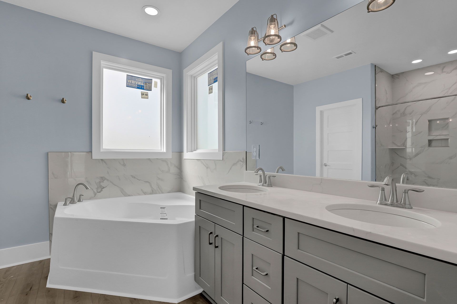 A light blue bathroom with a white tub, gray vanity, and large mirror.