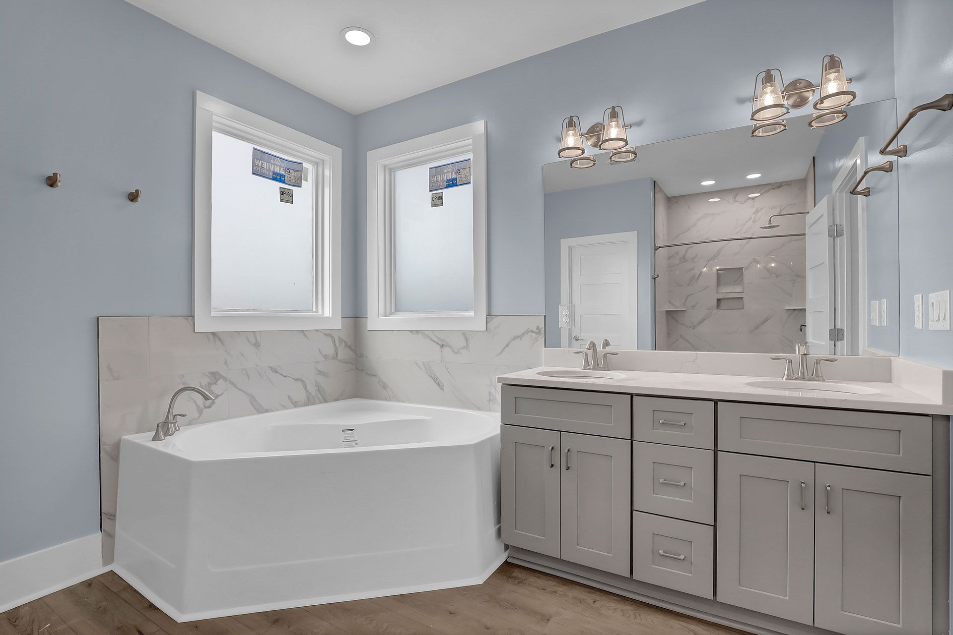 Bathroom with light blue walls, double vanity, and a corner bathtub.